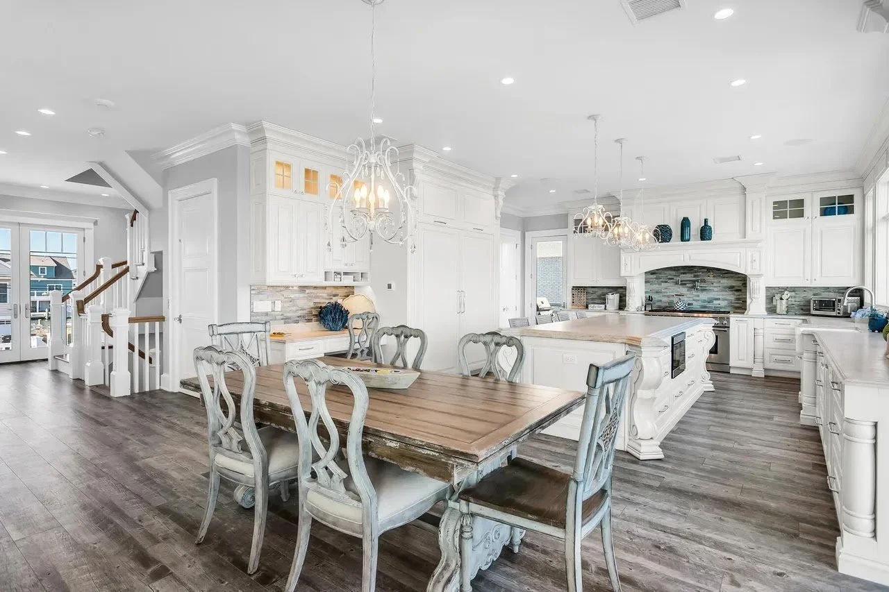 Spacious kitchen with white cabinets, a large island, wooden dining table, and hardwood floors.