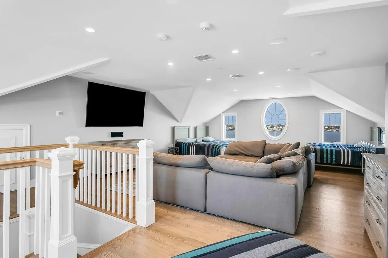 Upscale attic living space with vaulted ceiling, hardwood floors, large sectional sofa, two beds, and a flat-screen TV on the wall.