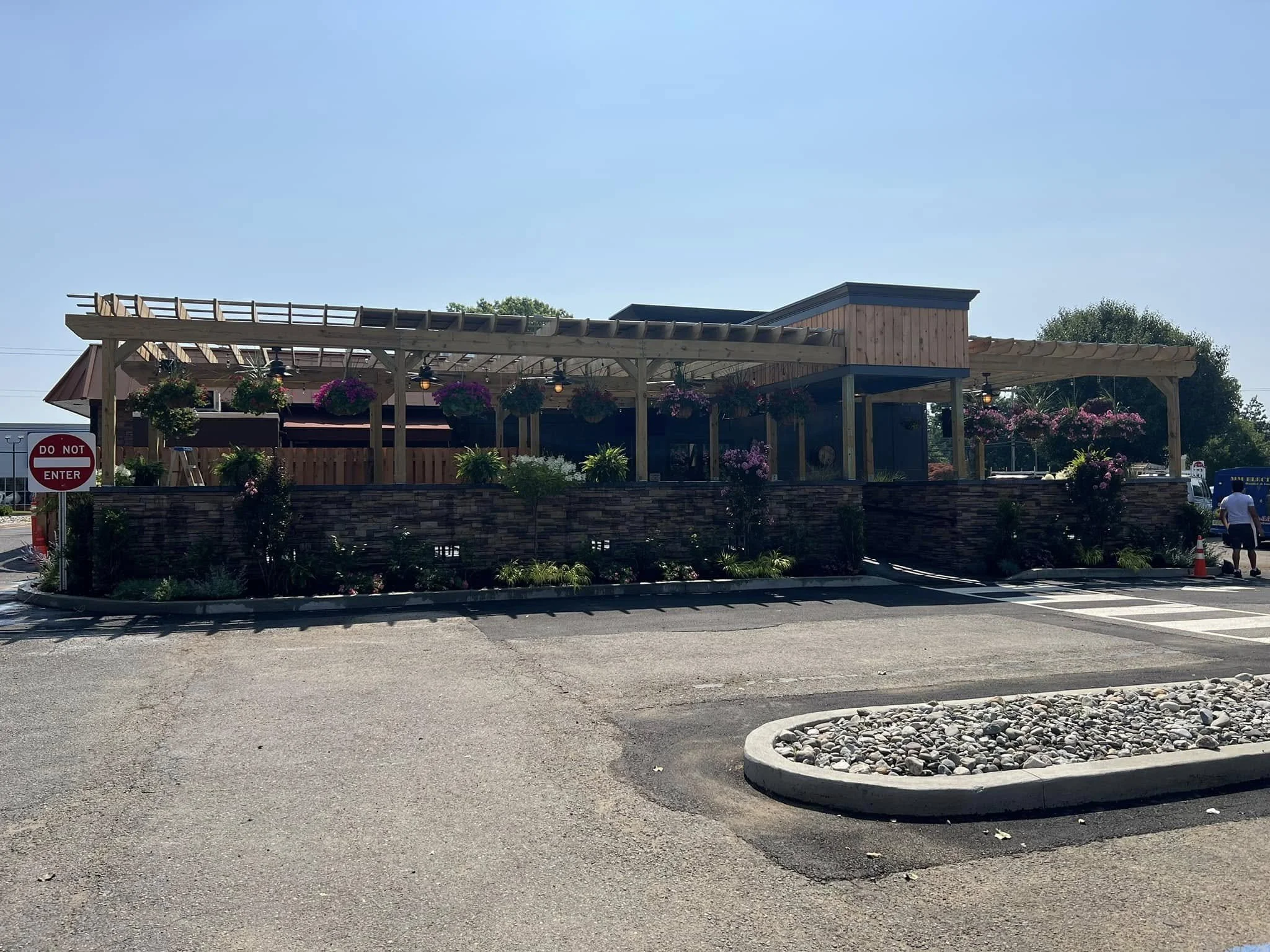 A restaurant patio with hanging flower baskets and a pergola, with a parking lot and a do not enter sign in the foreground.