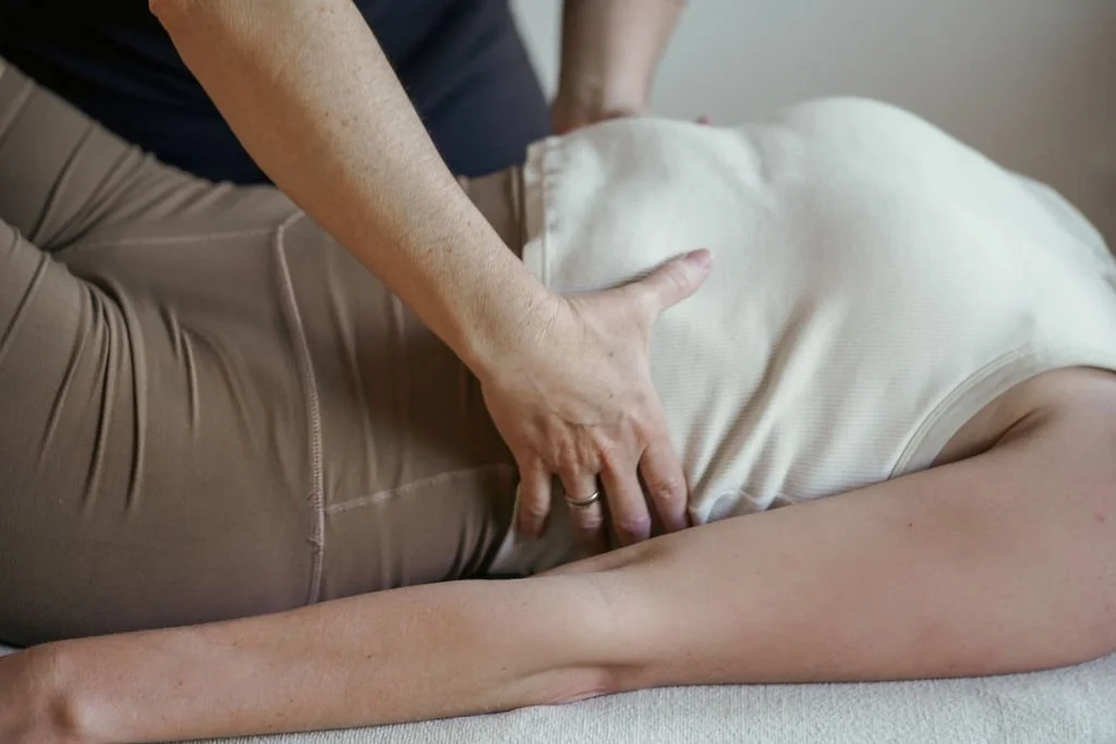 A person receiving chiropractic or physical therapy treatment, lying on their side, while another person applies pressure to their lower back.