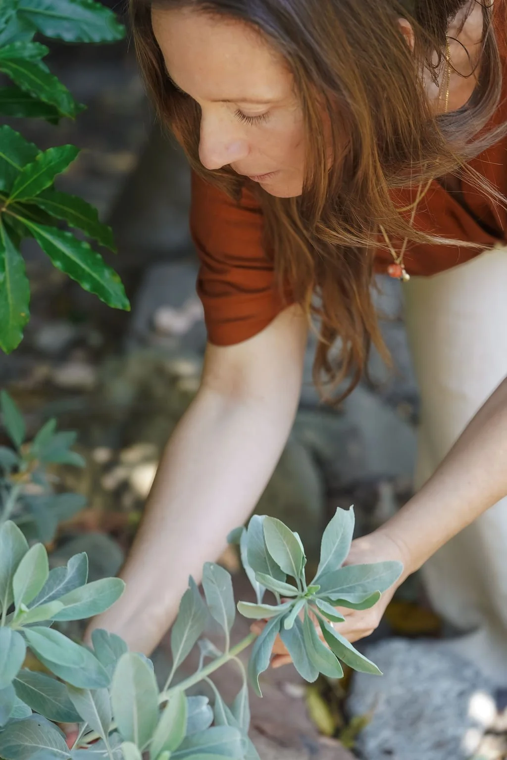 A woman with long brown hair tending to plants outdoors.