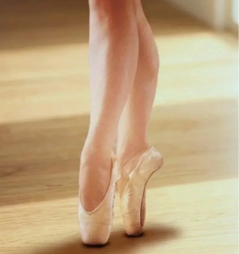 Close-up of barabara in her dancer legs and feet in pink ballet slippers on a wooden floor.