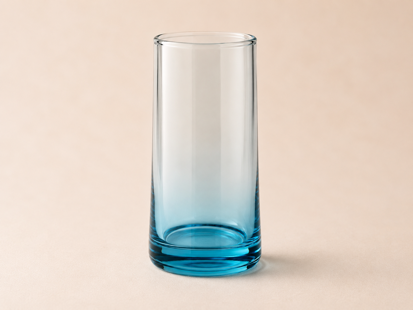 A clear glass with a blue tint at the bottom, empty, on a beige background.