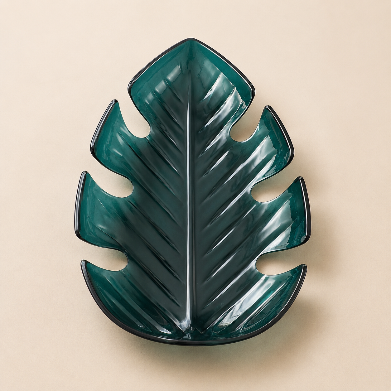 A dark green, ceramic decorative dish shaped like a monstera leaf, placed on a beige background.