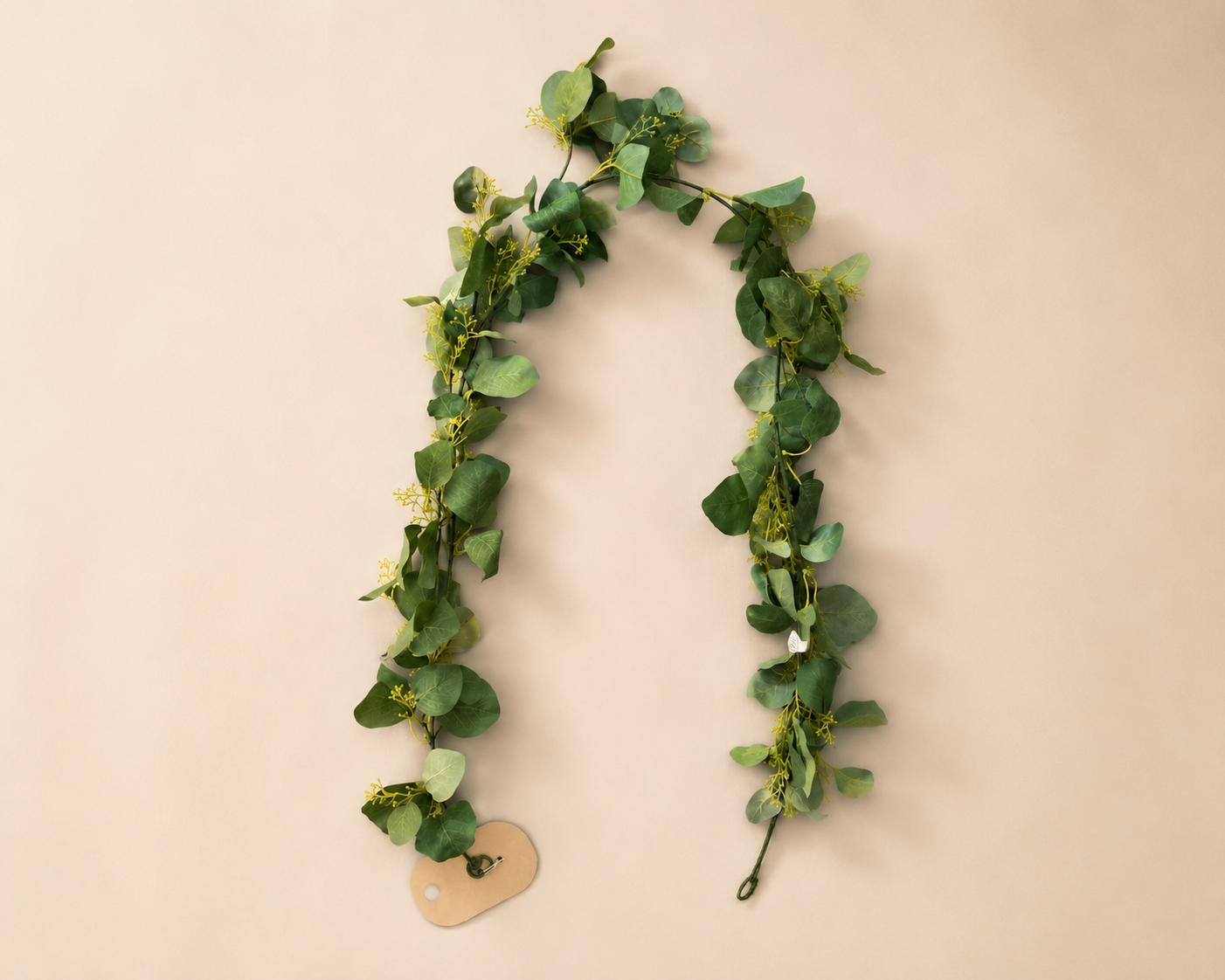 Artificial greenery hanging decoration with green leaves and small yellow flowers, attached to a beige wall.