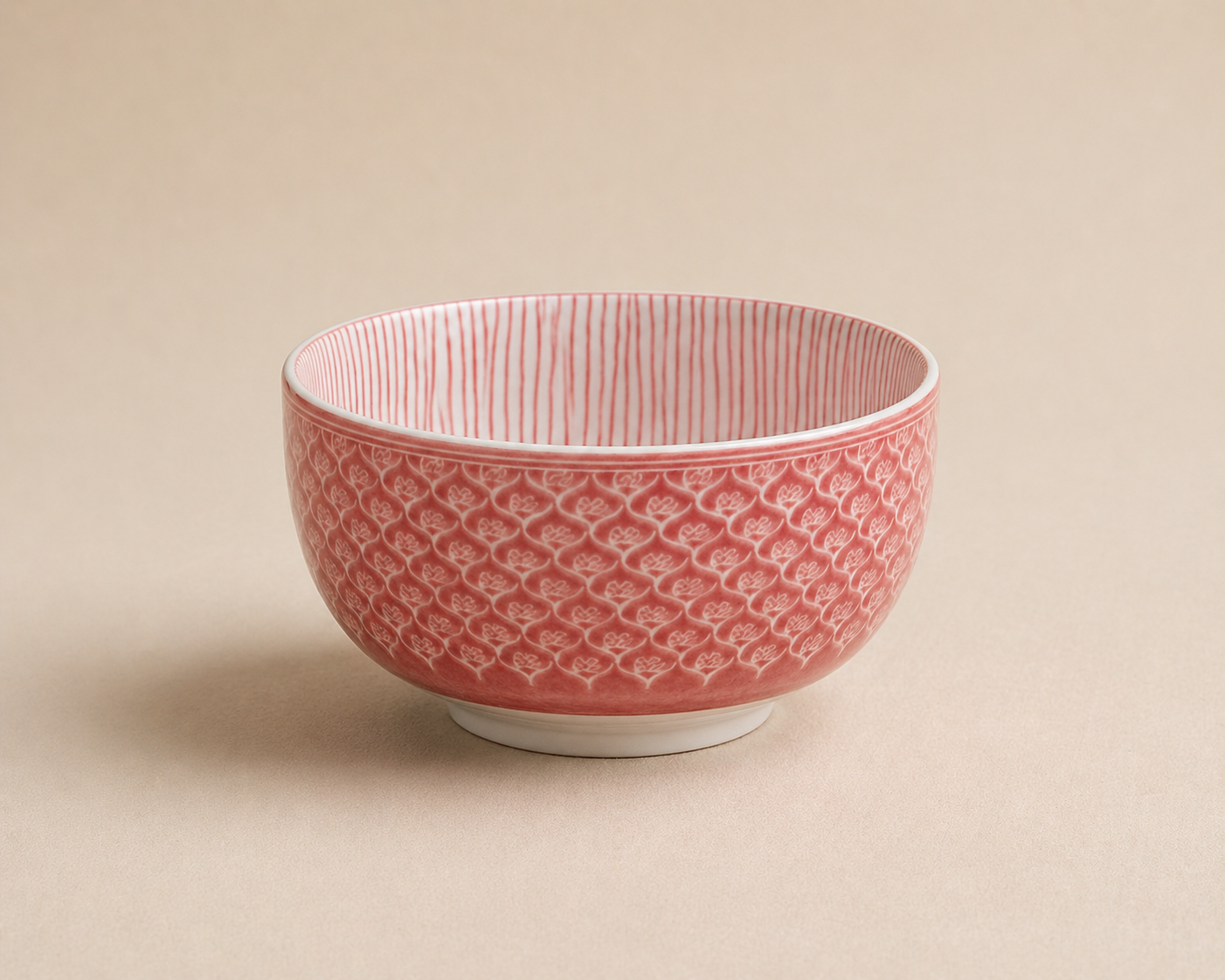 A pink and white ceramic bowl with a textured heart pattern on the exterior and vertical stripes on the interior, placed on a beige background.