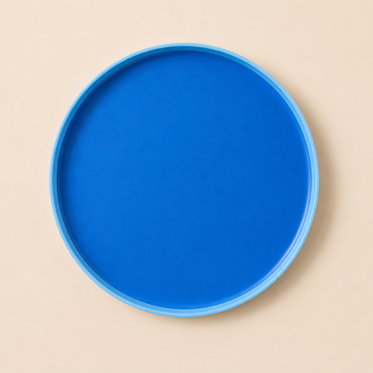 A round, blue plastic tray with a raised edge, placed on a plain beige surface.