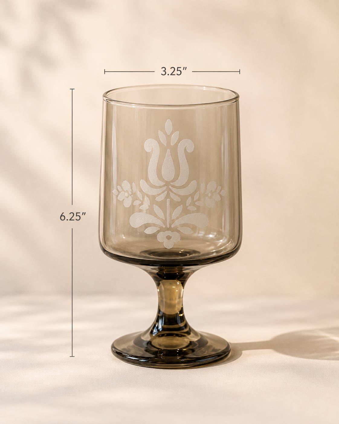 A clear glass goblet with a floral and abstract design etched on it, measuring 6.25 inches in height and 3.25 inches in top diameter, placed on a white surface against a plain background.