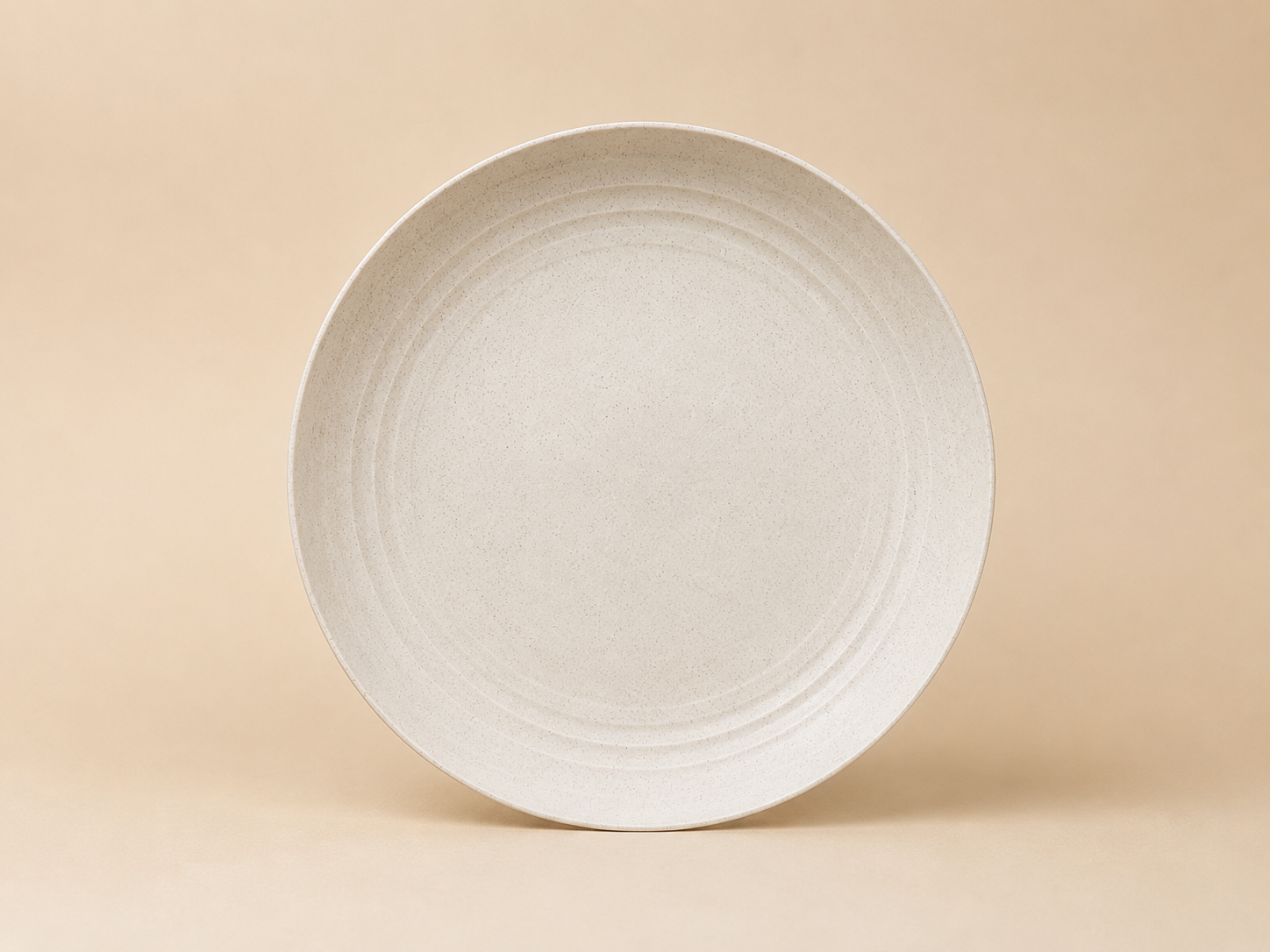 A round, off-white ceramic plate with a subtle speckled pattern, placed against a plain beige background.