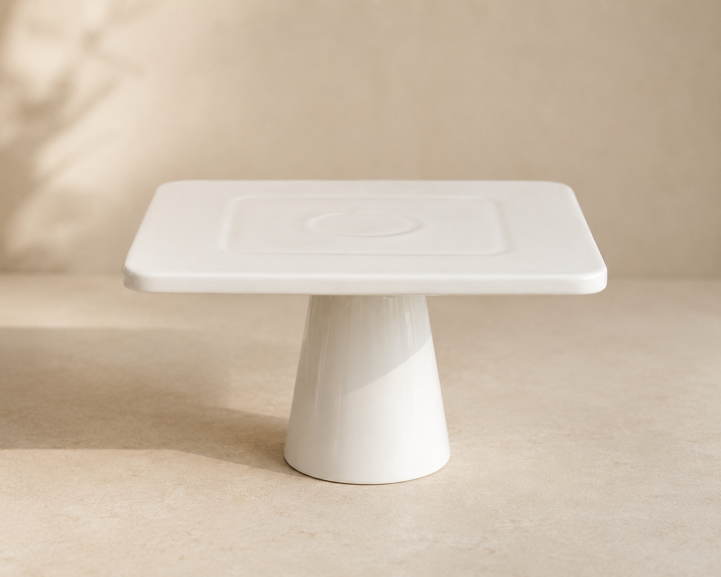 White rectangular ceramic soap dish with a slightly sloped surface, resting on a conical pedestal base, placed on a beige surface with a neutral background.