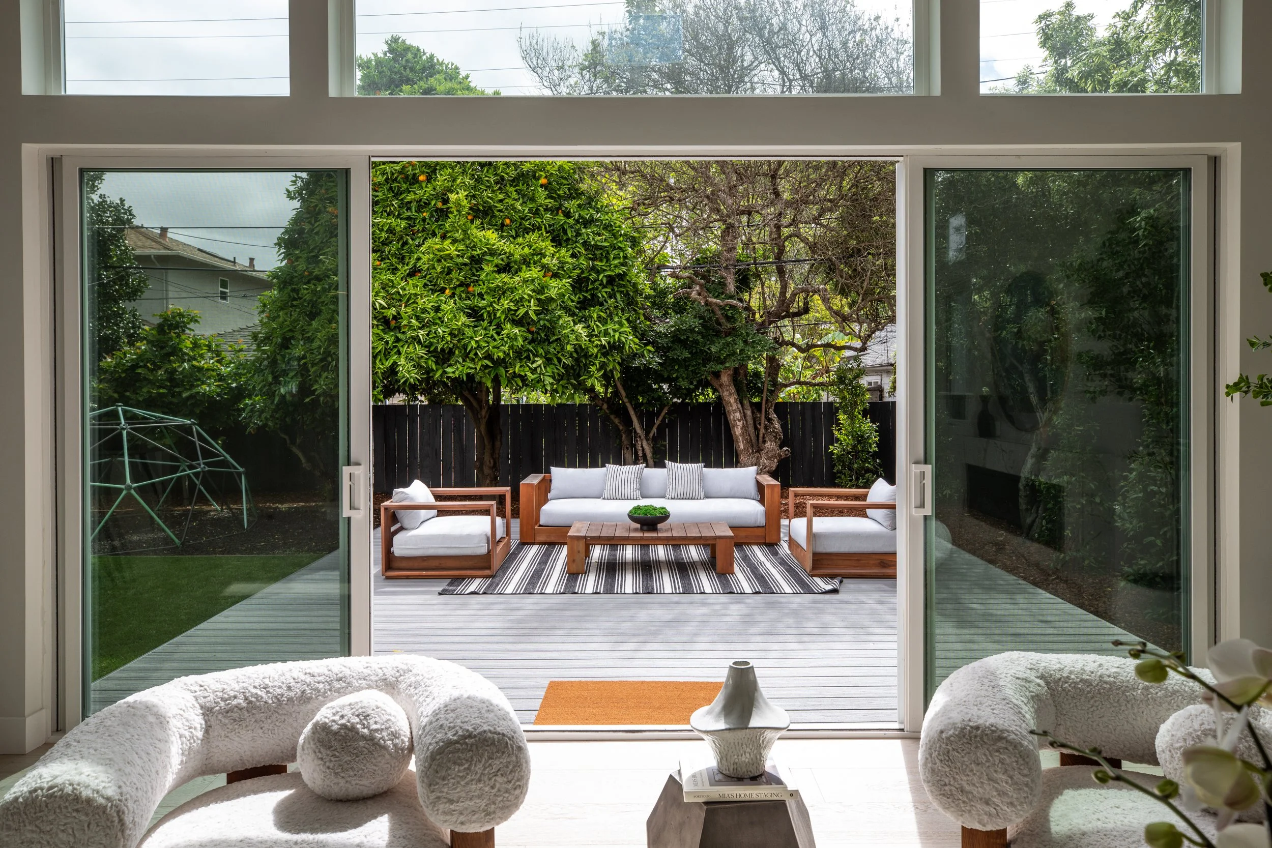 View of a living room with large sliding glass doors leading to an outdoor patio with seating and greenery.
