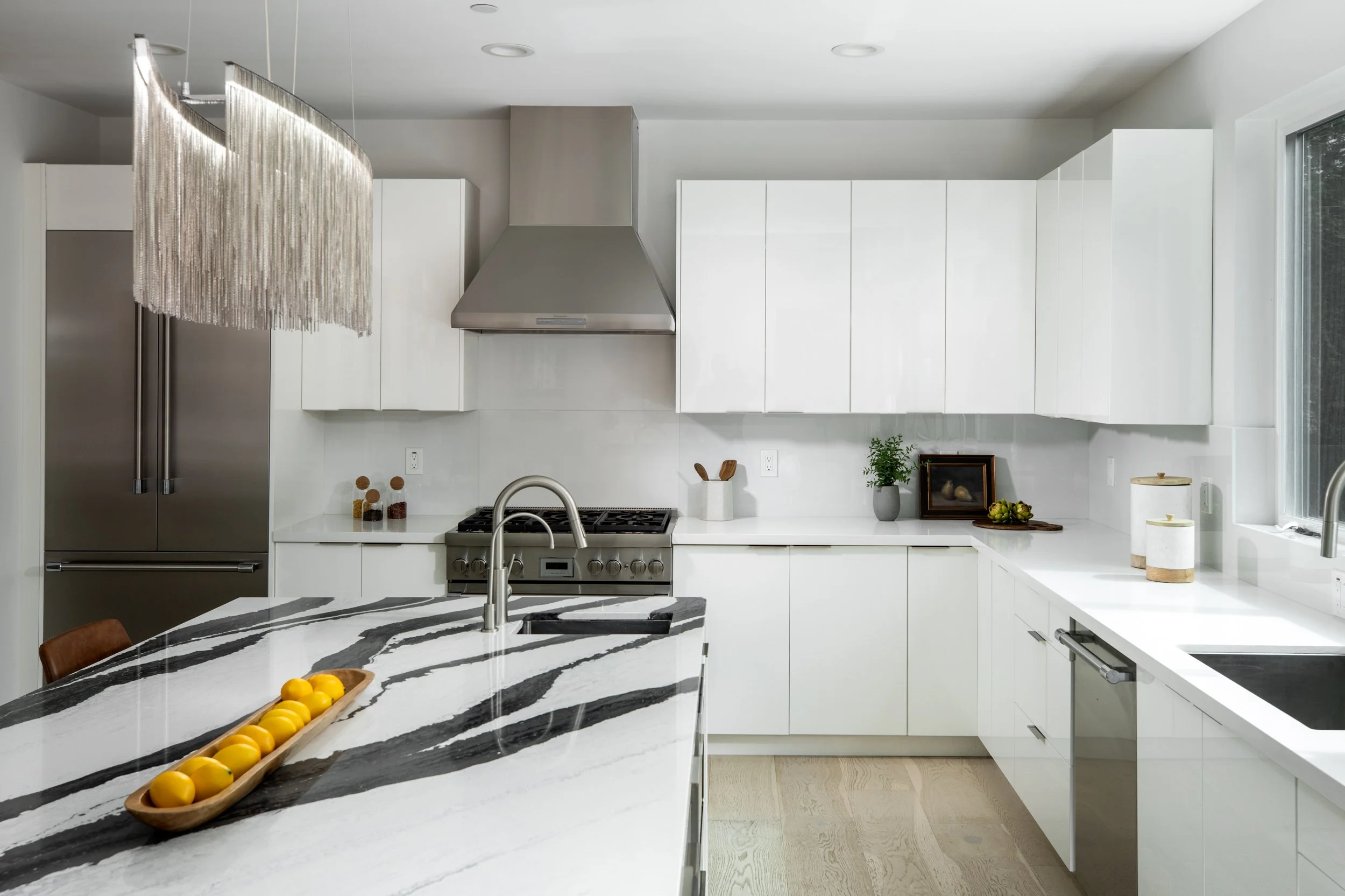 Modern kitchen with white cabinets, marble island, stainless steel appliances, and a large window.