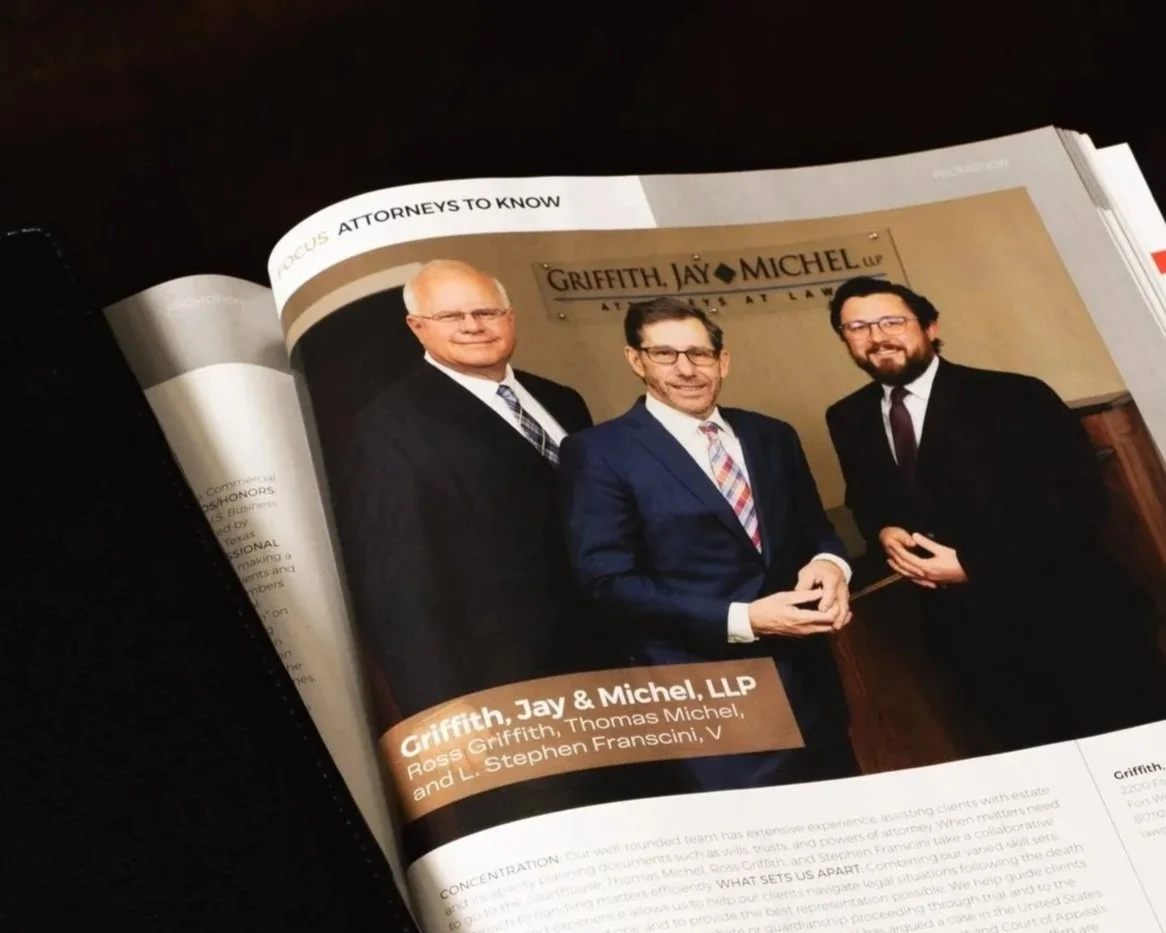 A magazine page featuring a photograph of three men in suits, standing in front of a sign that reads 'Griffith, Jay & Michel LLP, Attorneys at Law.' The caption below identifies them as Ross Griffith, Thomas Michel, and L. Stephen Francini.