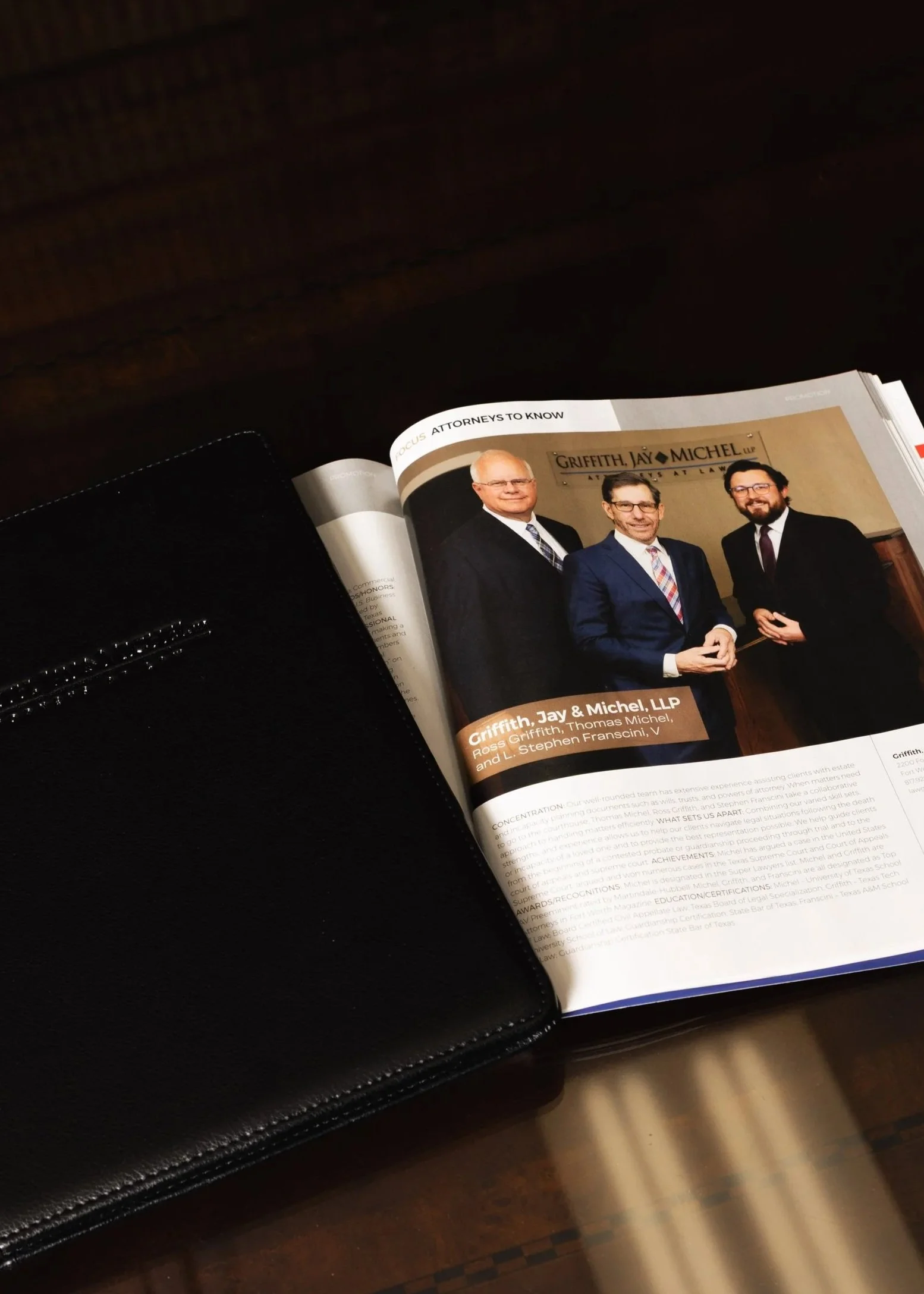 Open magazine page featuring a photo of three men in business suits standing together, with a sign reading 'Griffith, Jay & Michel LLP' in the background, and sections of text below.