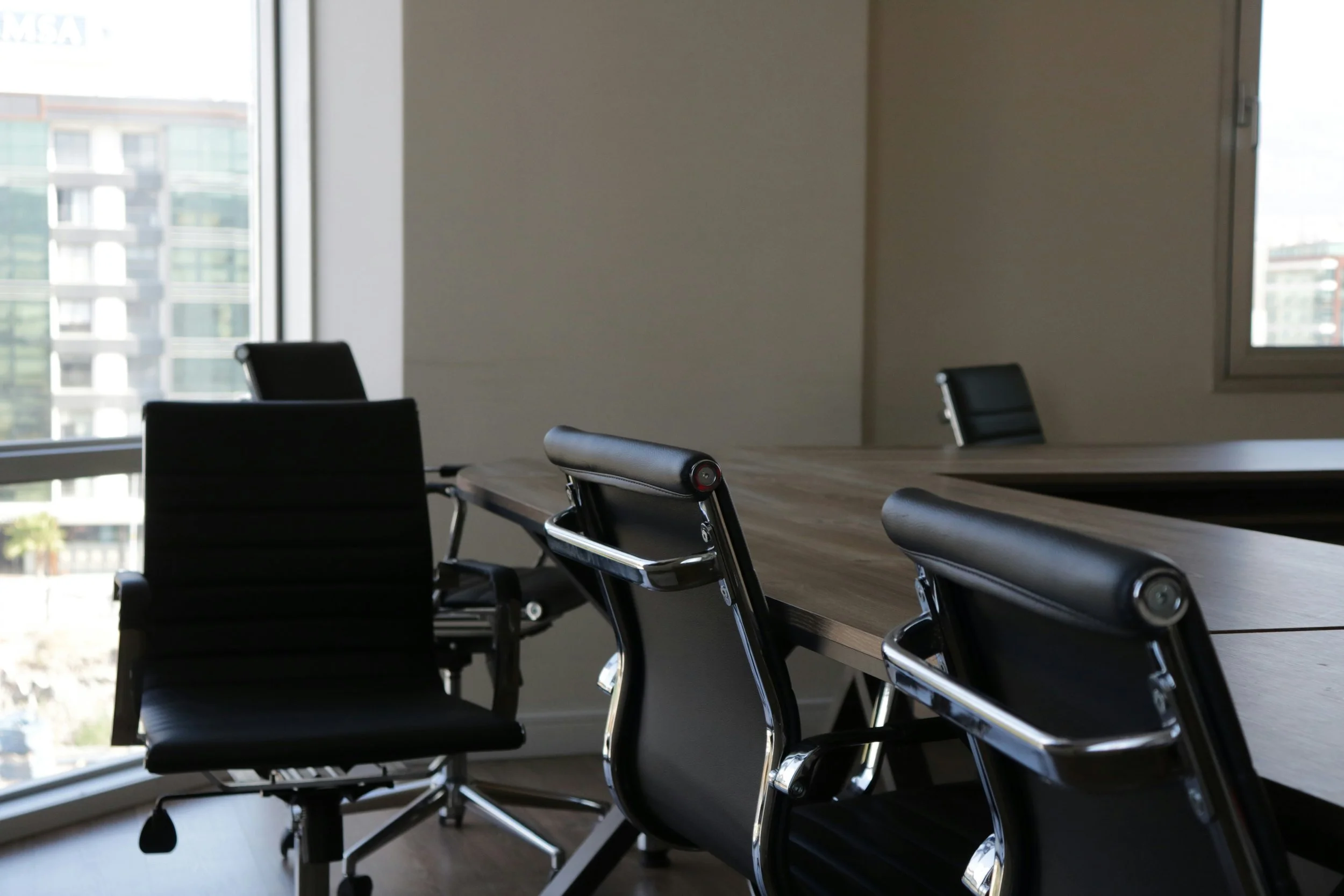 Empty conference room with large windows and black office chairs around a long table.