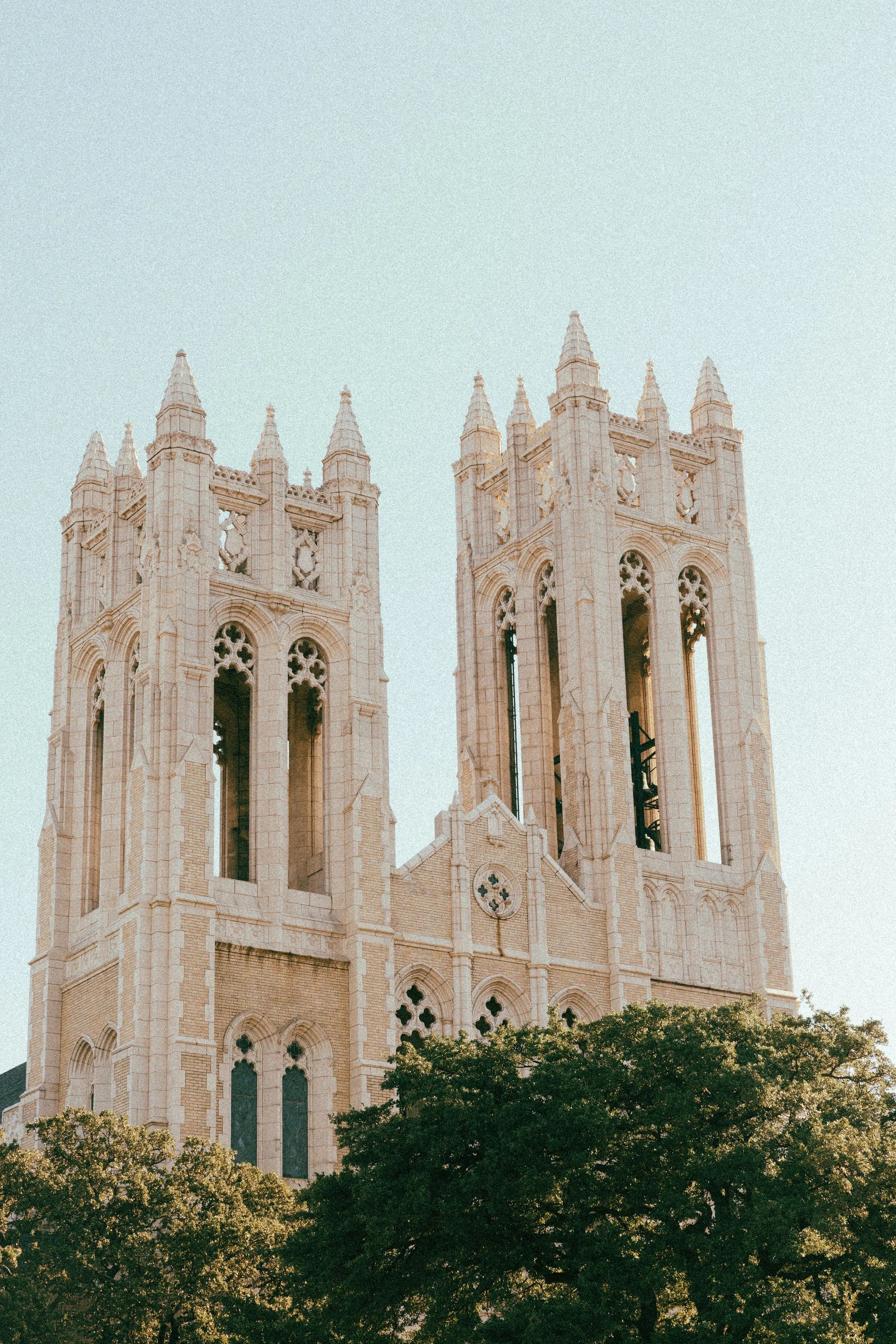 Gothic-style church towers with large ornate windows and pointed spires, surrounded by green trees.