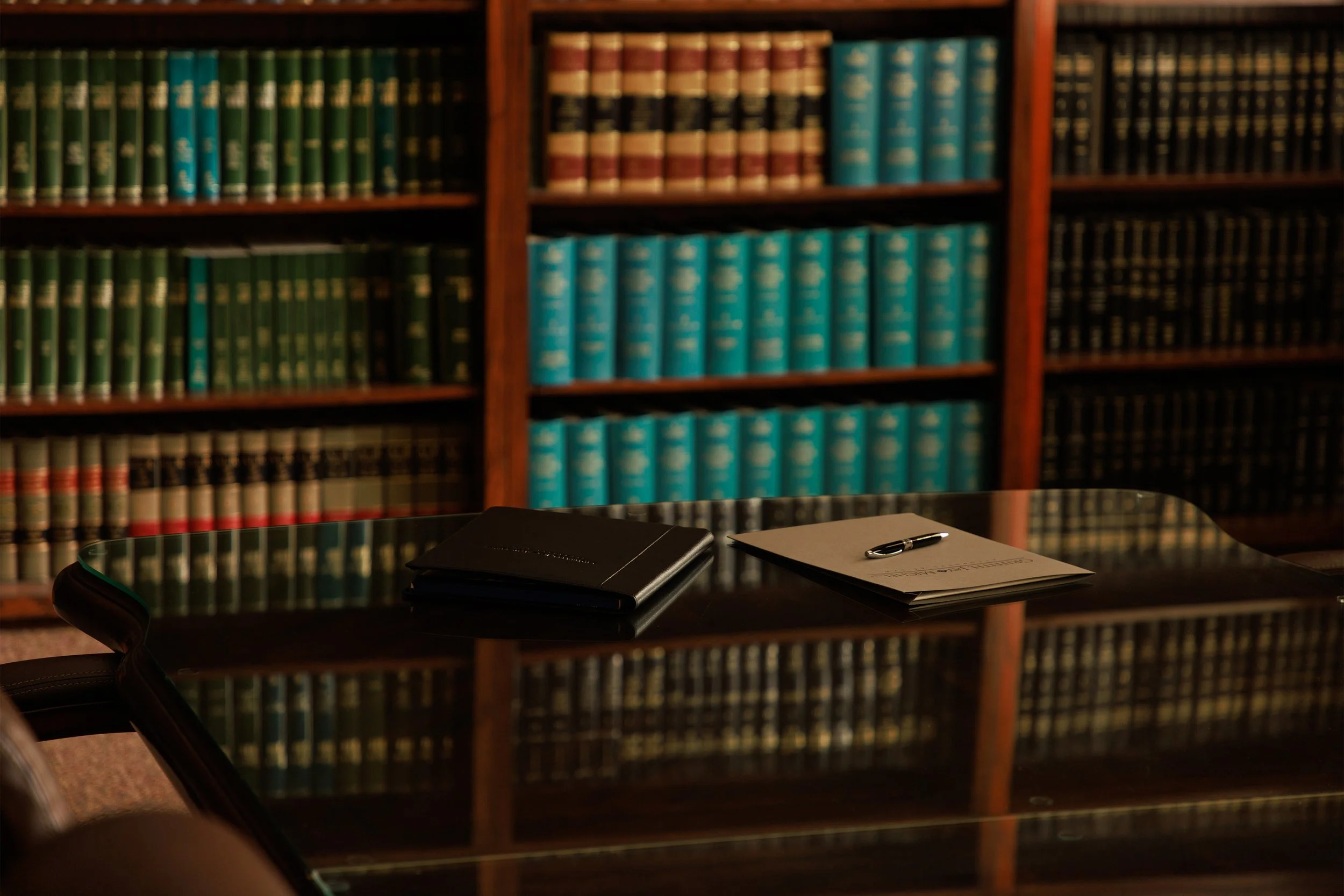 A wooden bookshelf filled with green, brown, and black law books in a library room.