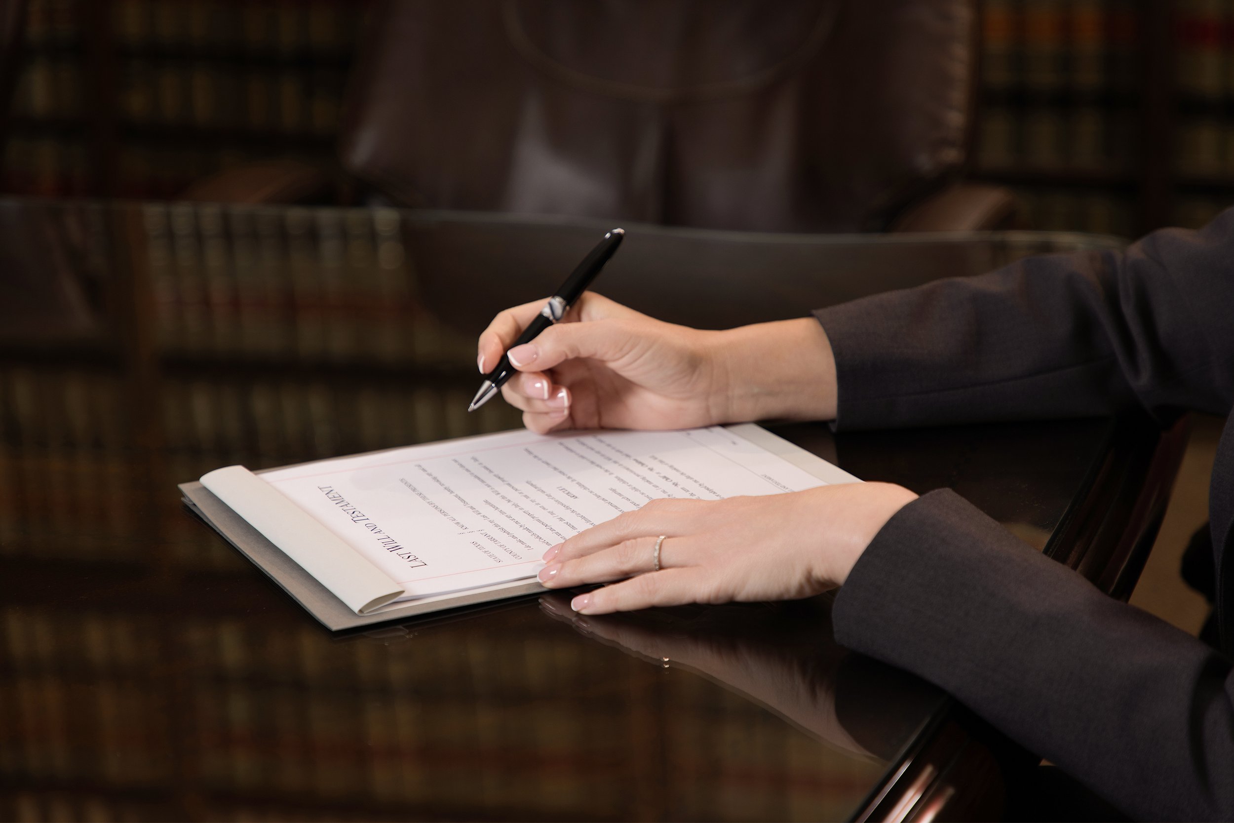 A person in formal attire sitting at a table, reading a document titled "Leslie A. Westphal at the University of California" with a pen in hand, in a library setting.