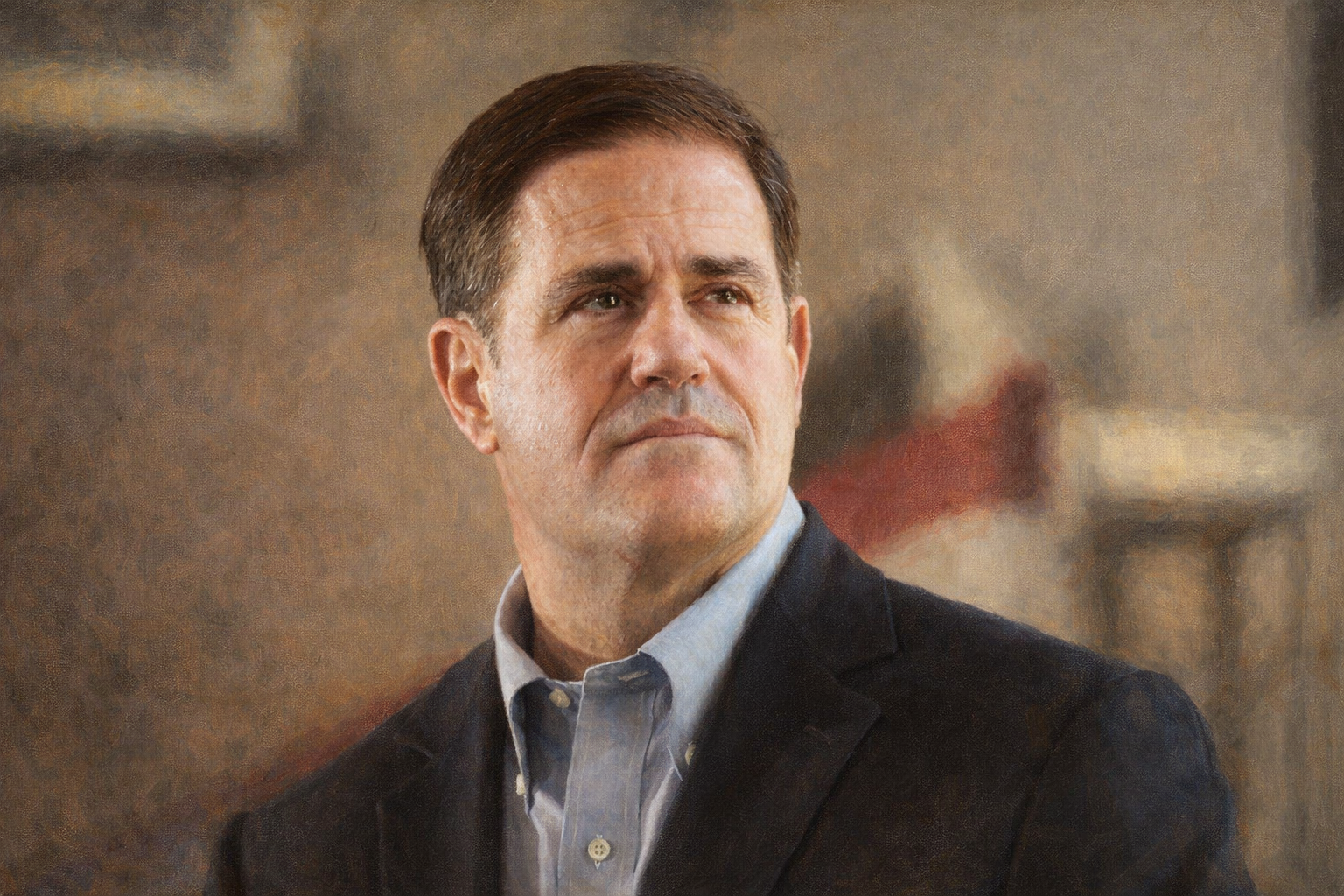 A middle-aged man with short dark hair and a serious expression, wearing a dark blazer and a light-colored collared shirt, looking slightly to the side in an indoor setting.