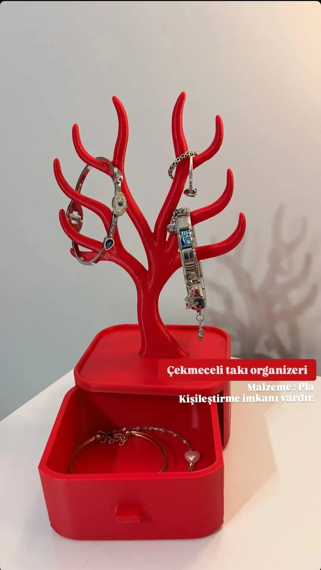 Red jewelry organizer shaped like a tree with jewelry hanging on its branches, placed in a matching red box. Text on image describes it as a bracelet jewelry organizer made of plastic with customization options.