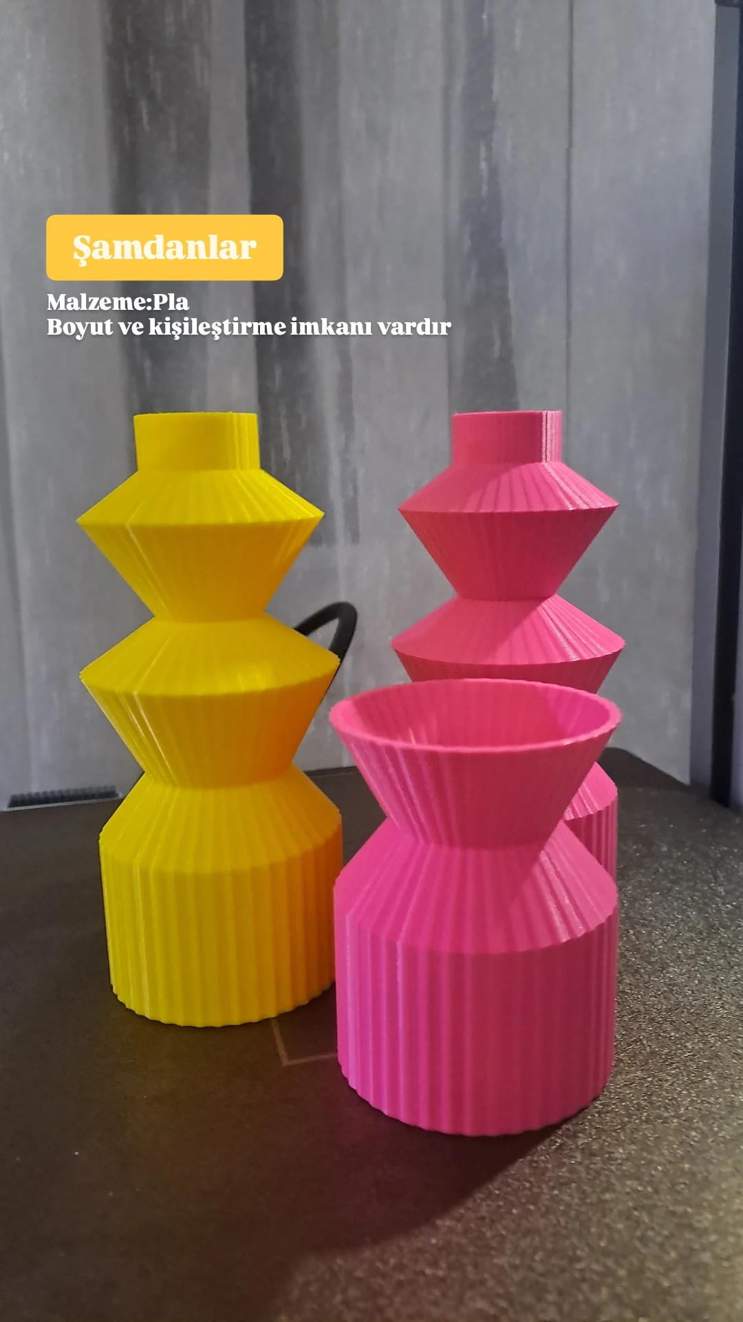 Colorful plastic vases in yellow and pink with ribbed, geometric designs, placed on a dark surface against a gray wall.