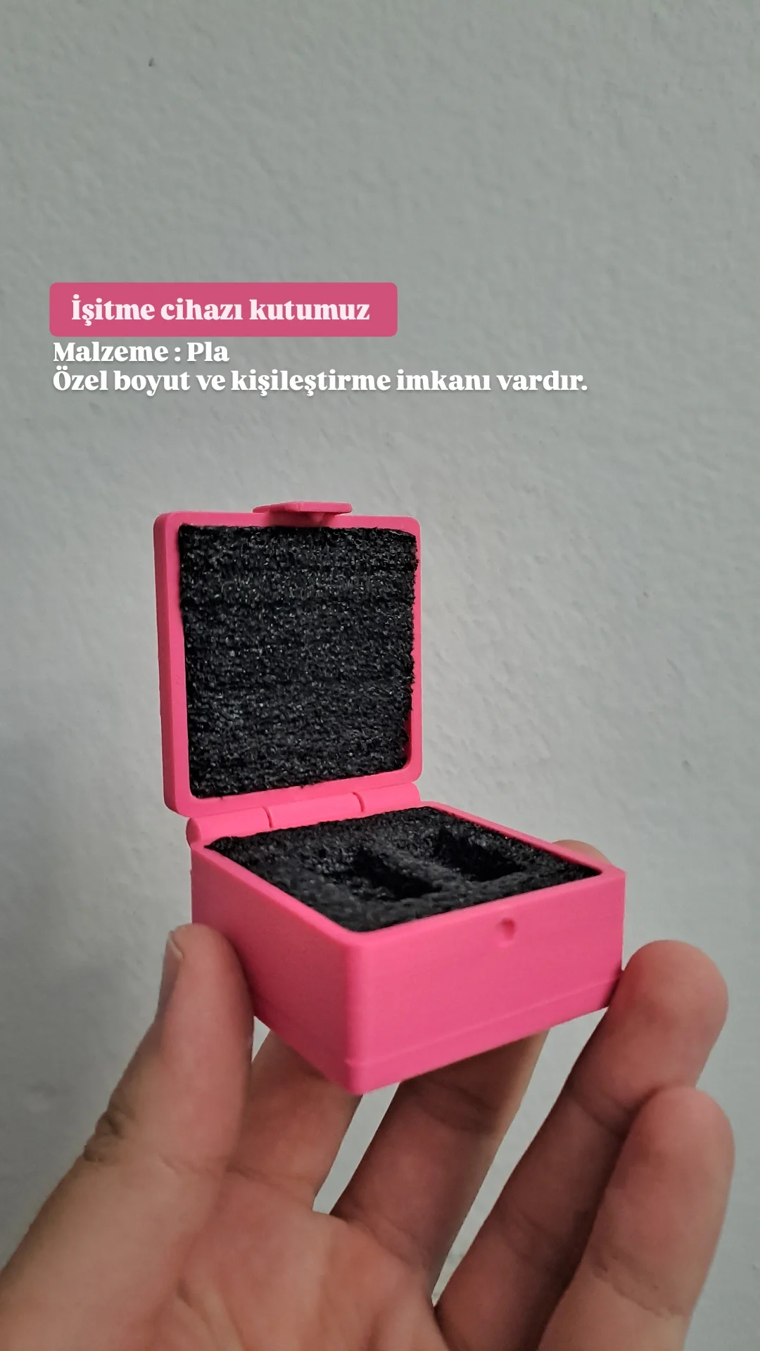 Hand holding a pink hearing aid case open with black foam interior and Turkish text explaining it as a hearing aid case made of PLA, customizable in size and personalization.