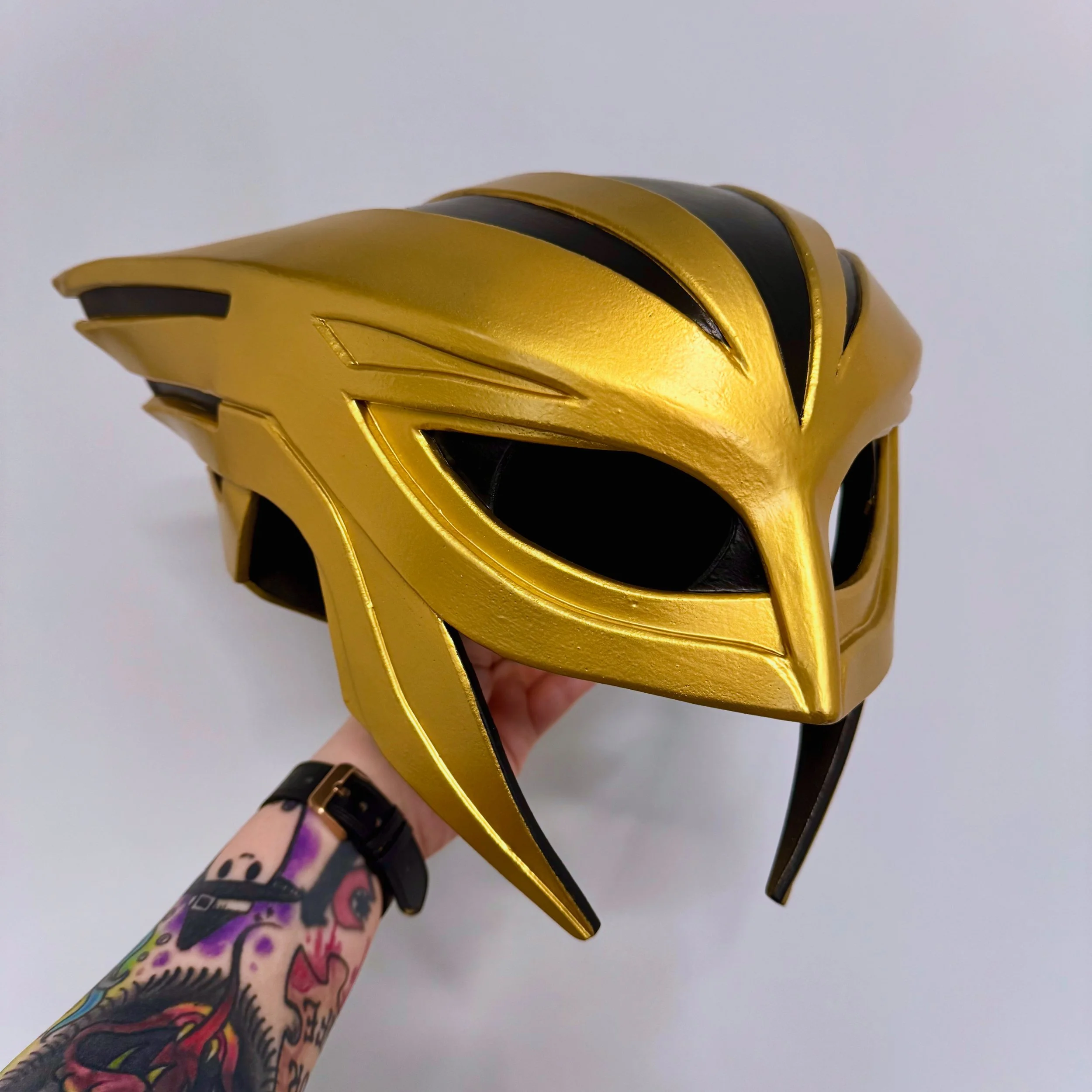 Hand holding a yellow and hawkgirl superhero helmet with a white background.