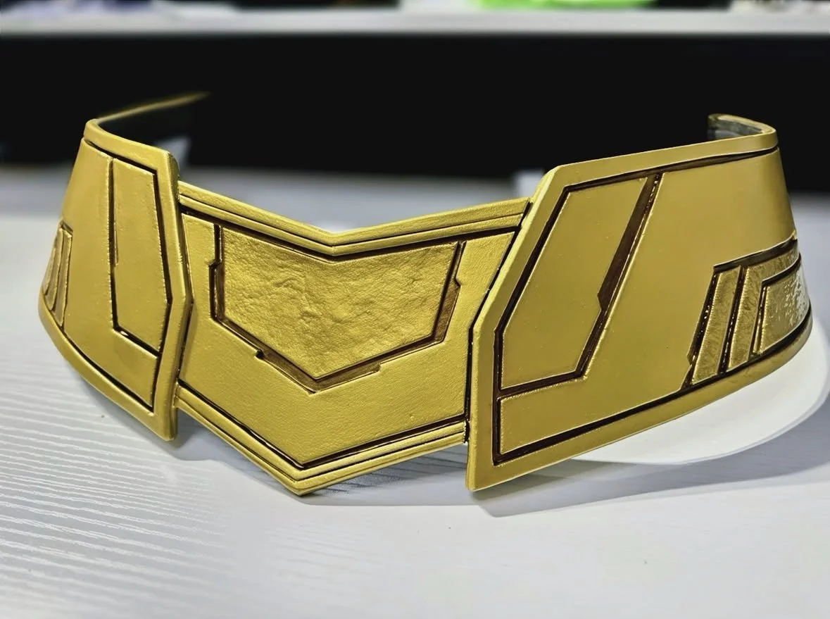 A gold-colored, futuristic-style belt with angular geometric patterns on a white surface for the superhero Supergirl