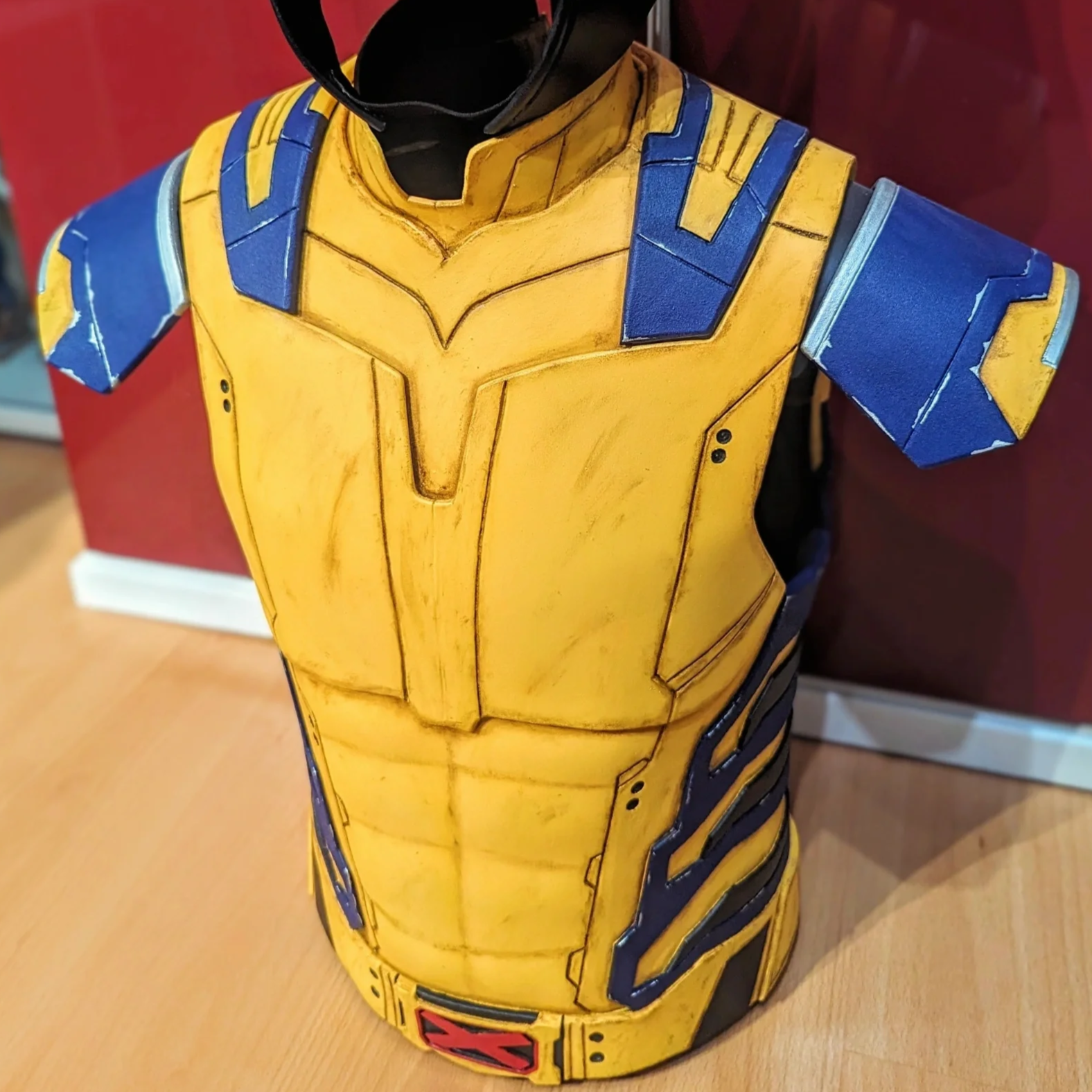 A yellow and blue costume armor, resembling Wolverine's superhero suit, with detailed lines and a stylized chest plate, displayed indoors.