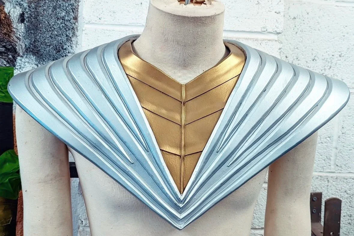 A mannequin wearing a futuristic costume with a golden front piece and a silver, layered collar that resembles armor.