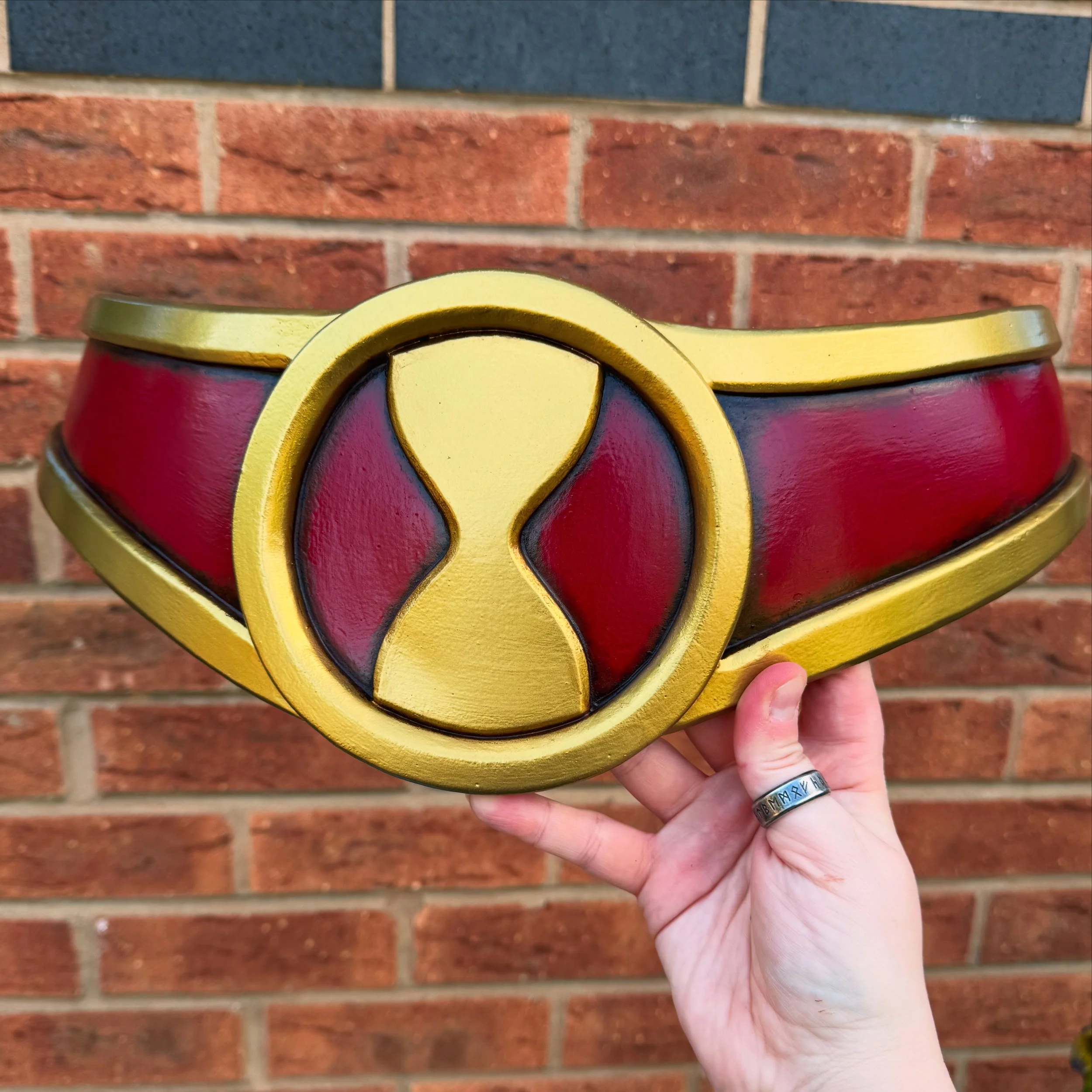 Close-up of a decorative object depicting a red and gold superhero belt with an hourglass logo on the front
