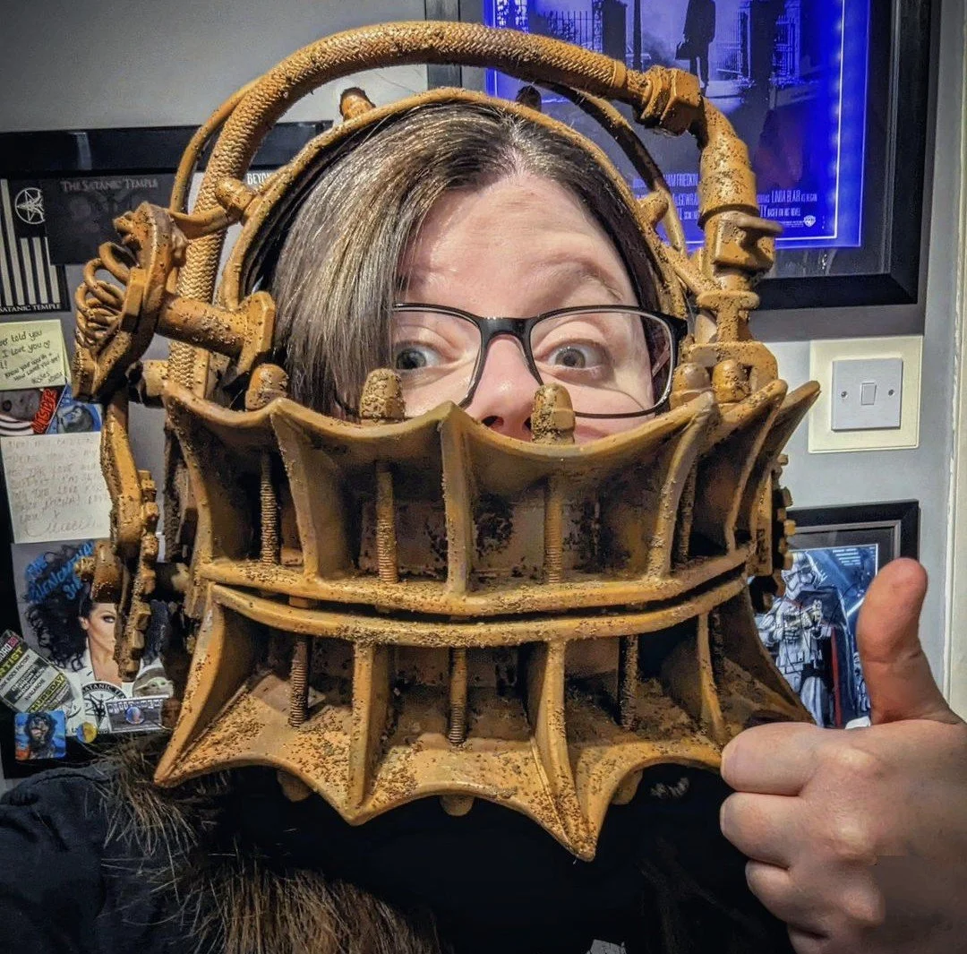Person looking through a reverse bear trap from the Saw movies, giving a thumbs-up gesture.