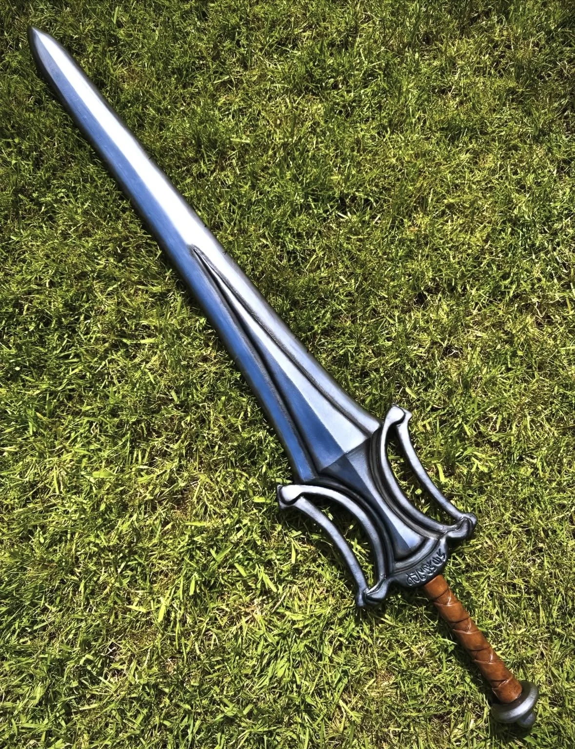 A sword with a silver blade and ornate hilt lying on green grass.