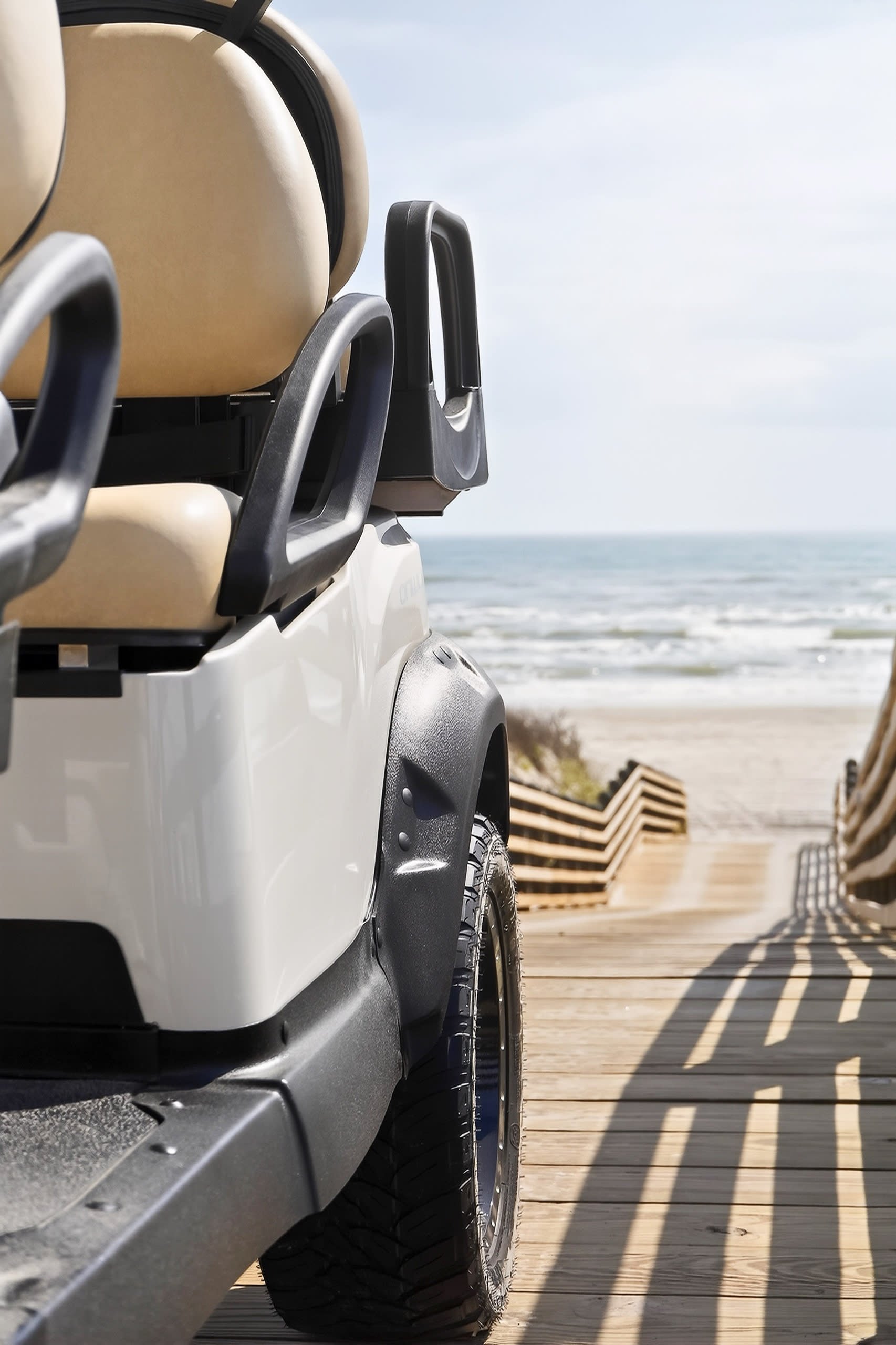 A close-up of an off-road vehicle parked on a wooden pier, with the ocean and sky in the background, including a row of lounge chairs.
