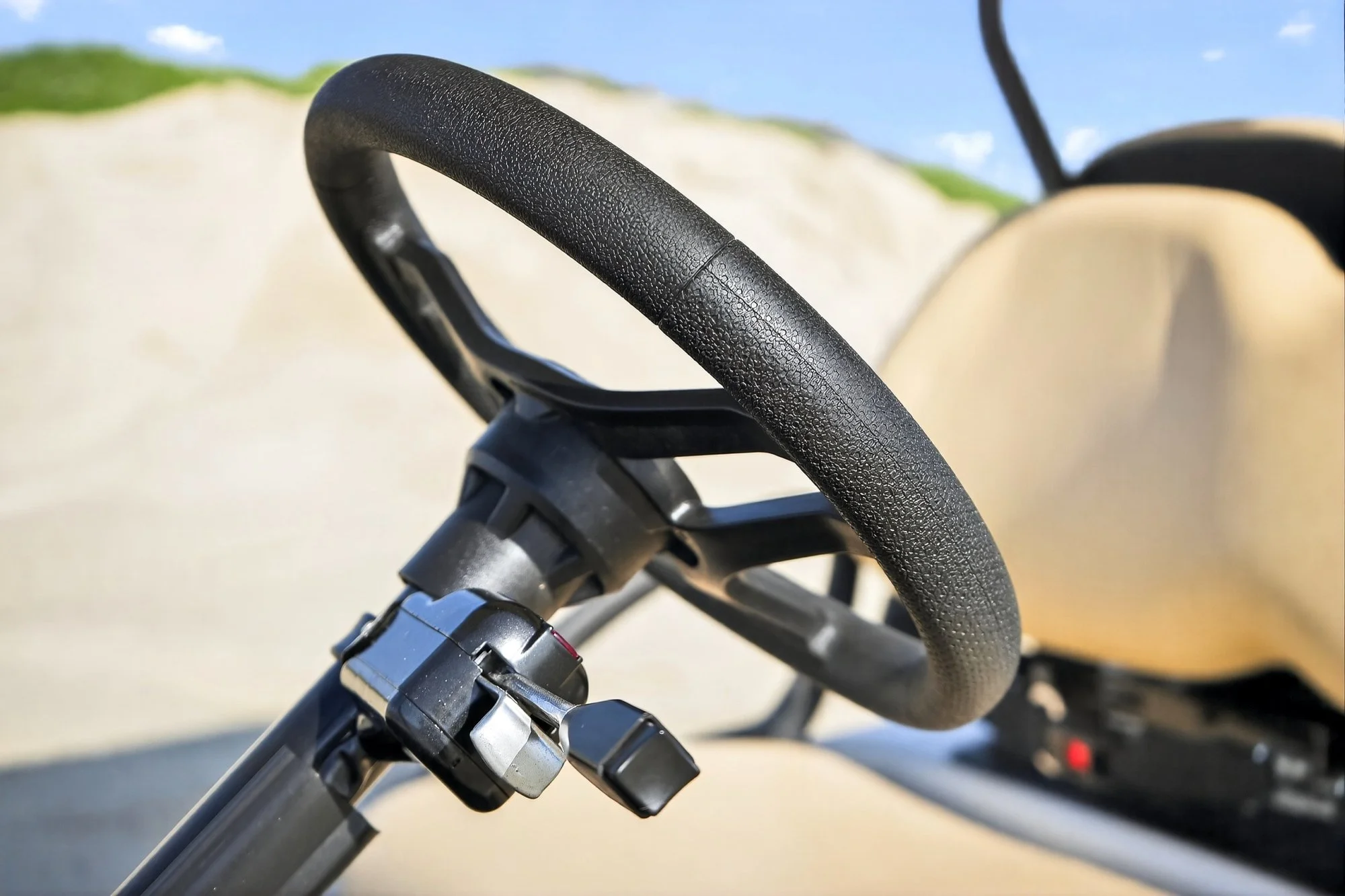 Close-up of a black bicycle handlebar with a textured grip, against a blurred background of a bright sky and green landscape.