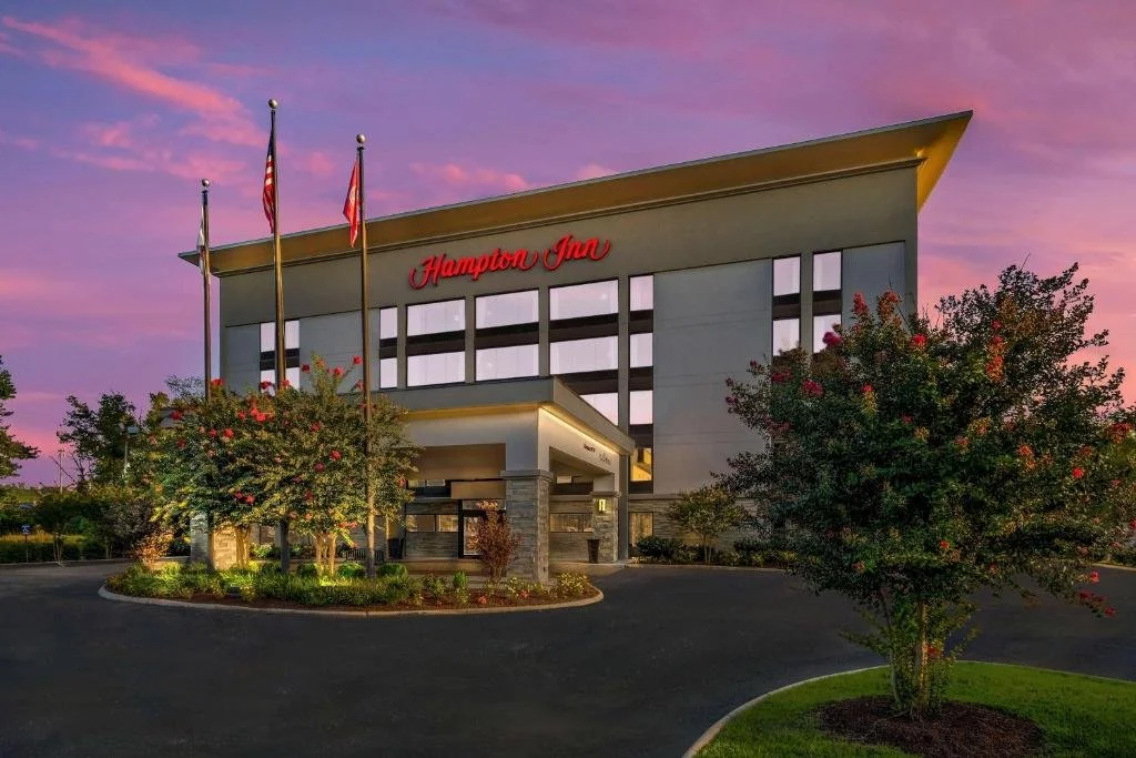 Hampton Inn hotel exterior at sunset with trees and a driveway