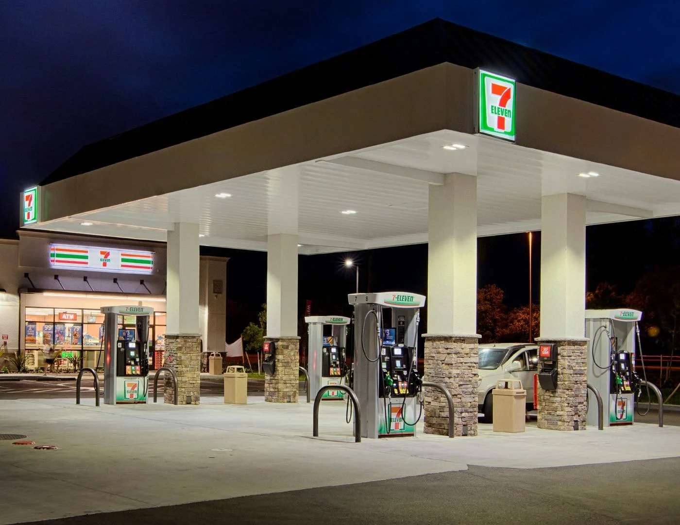 Night view of a 7-Eleven gas station with several fuel pumps and a convenience store in the background.