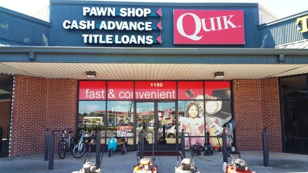 Front of a Quik convenience store with signs for pawn shop, cash advance, and title loans above the entrance. The window has advertising with a girl, and there are bicycles and scooters parked outside.