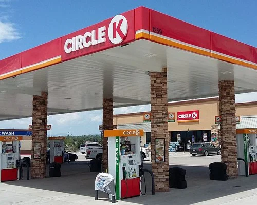 Circle K gas station with fuel pumps, brick pillars, and store in the background under a blue sky.