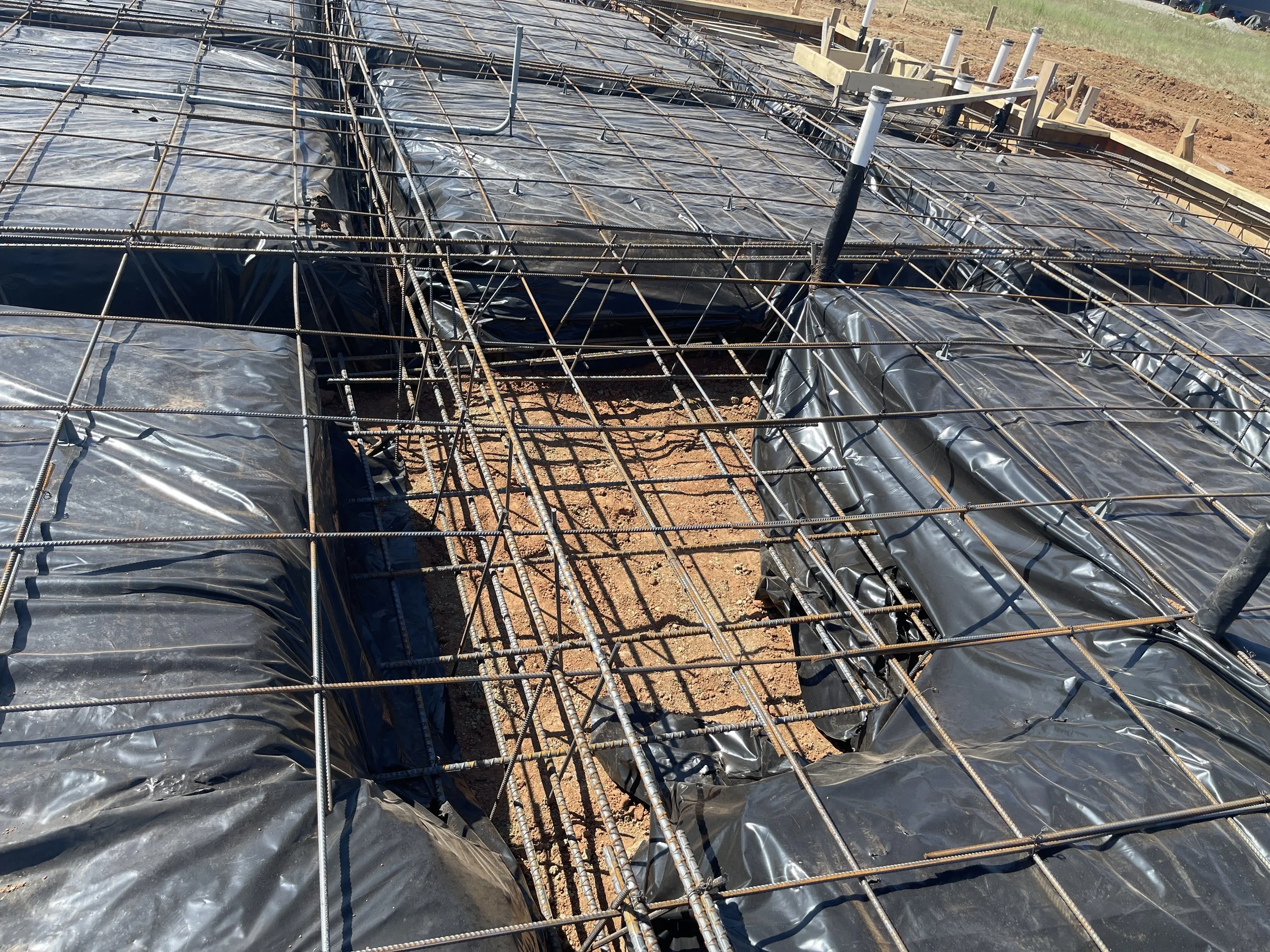 Construction site with rebar framework and black plastic sheeting covering concrete foundation.