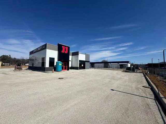 Empty parking lot outside a modern fast food restaurant with a large red logo and a portable toilet nearby.