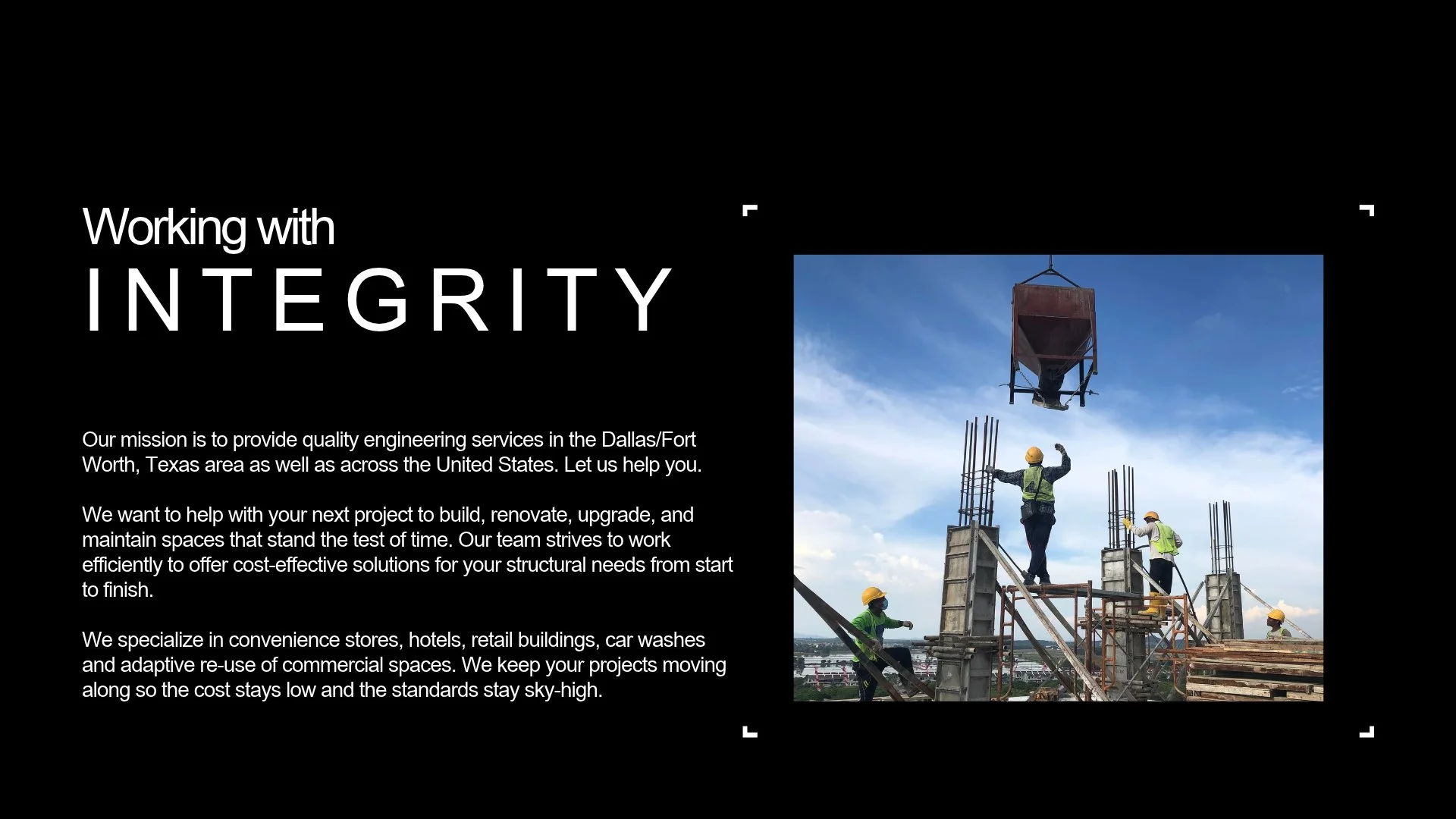 Construction workers wearing safety helmets and vests working on the building site, with one worker guiding the placement of a suspended container.