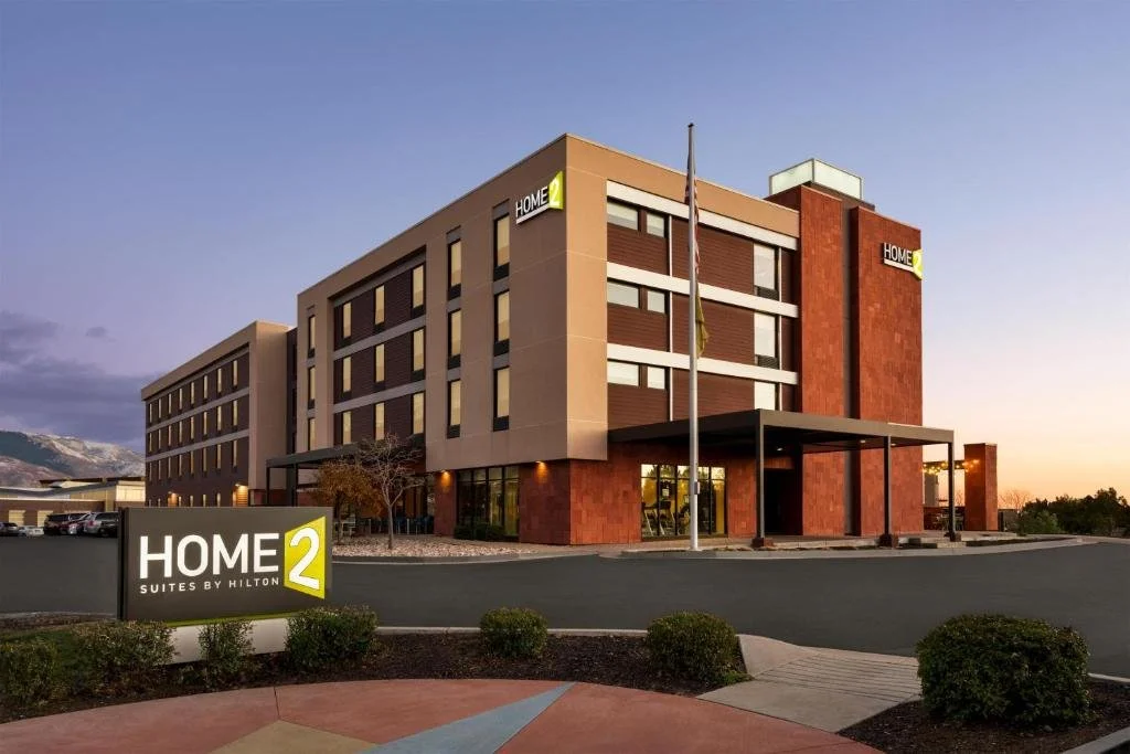 Exterior view of a Hilton Home2 Suites hotel building during sunset with a sign in the foreground.