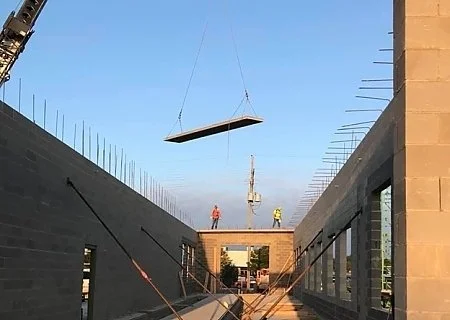 Construction workers guiding a large rectangular platform suspended by a crane between two concrete walls.