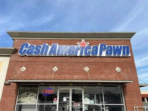 Exterior of a store named Cash America Pawn with a brick facade, large sign, and glass storefront showing an open sign and various items inside.