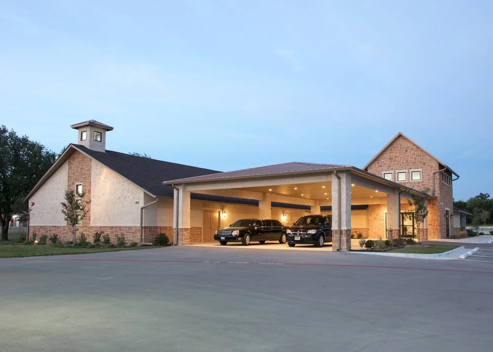 A modern church building with a covered parking area, cars parked underneath, and a brick and stucco exterior during dusk.