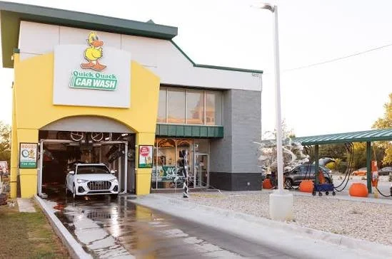 Auto detailing shop with a white car inside and outdoor self-serve wash stations with orange pumpkins.
