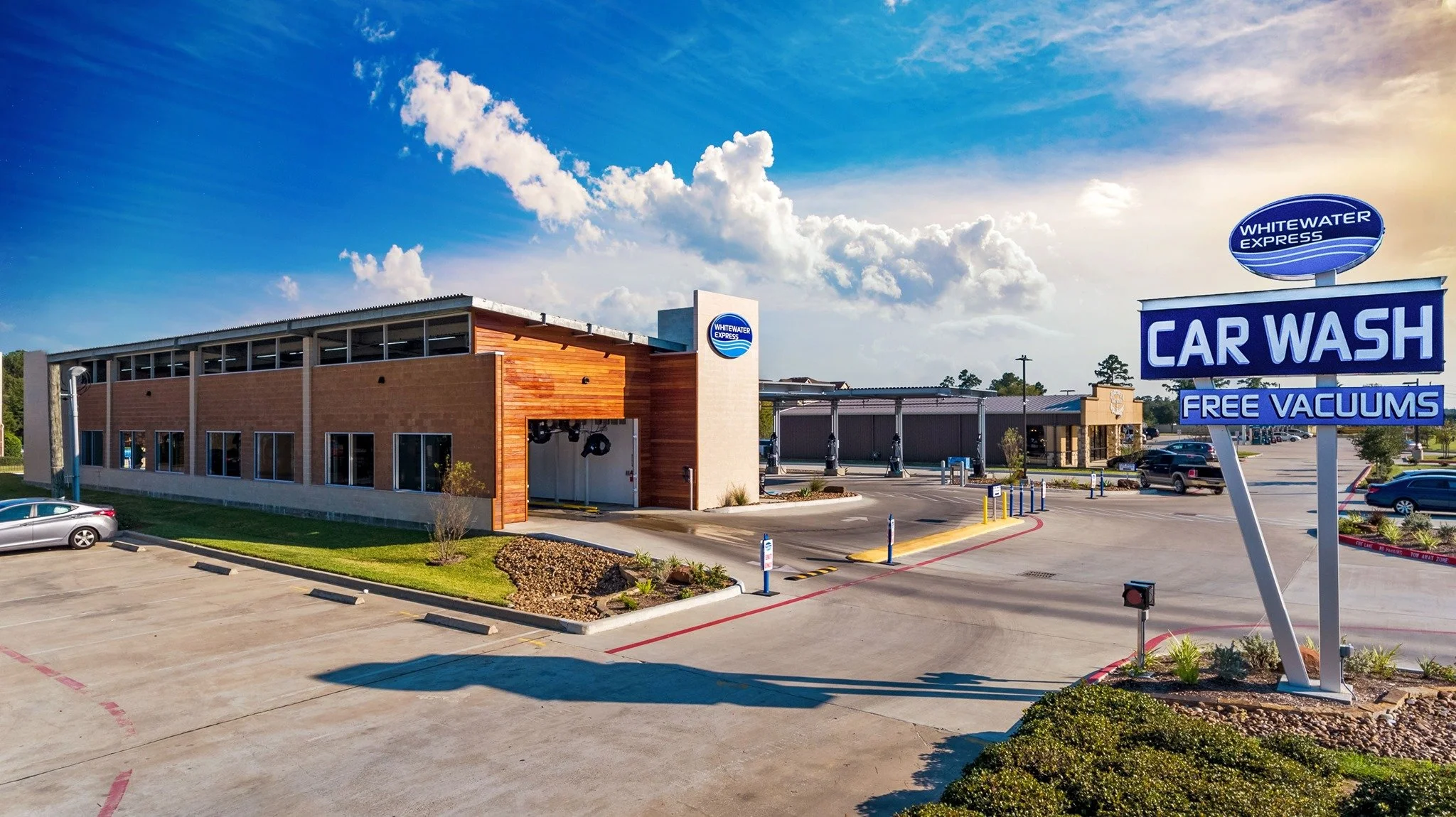 A car wash and vacuum station at a parking lot with a blue sky and clouds overhead.