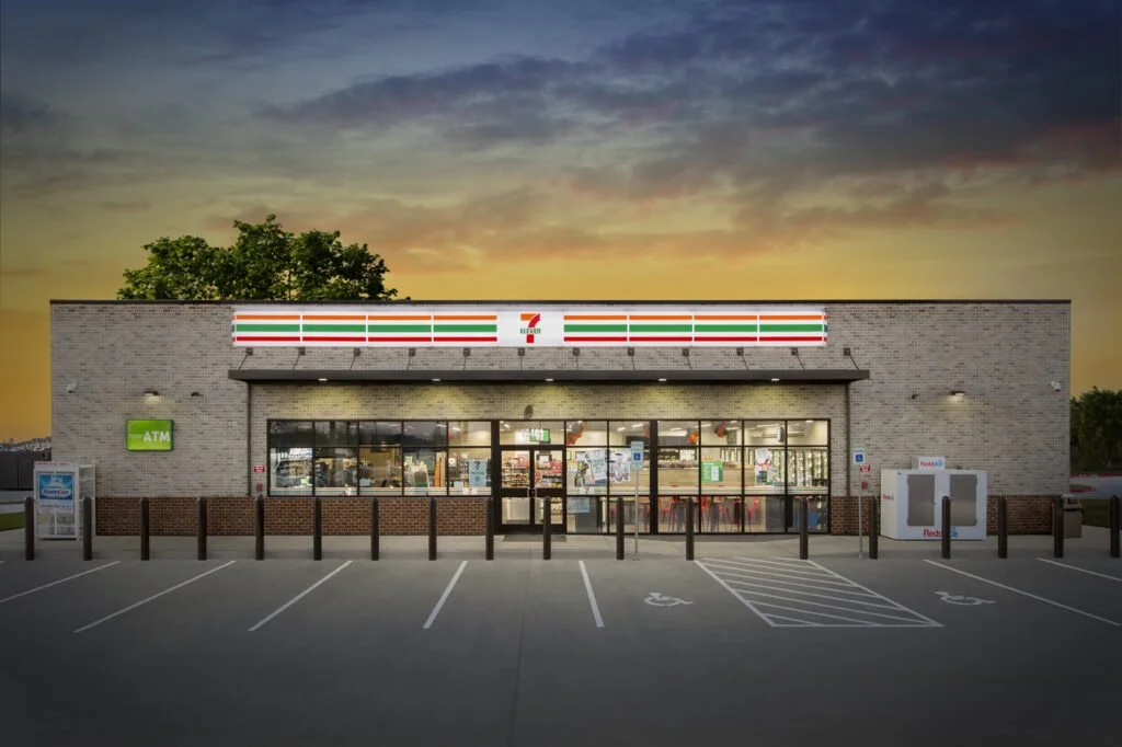 Exterior of a 7-Eleven convenience store at sunset, with parking spaces in the foreground.