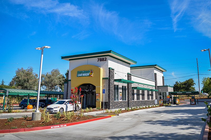 Quick Quack Car Wash building with parking lot and cars, clear blue sky